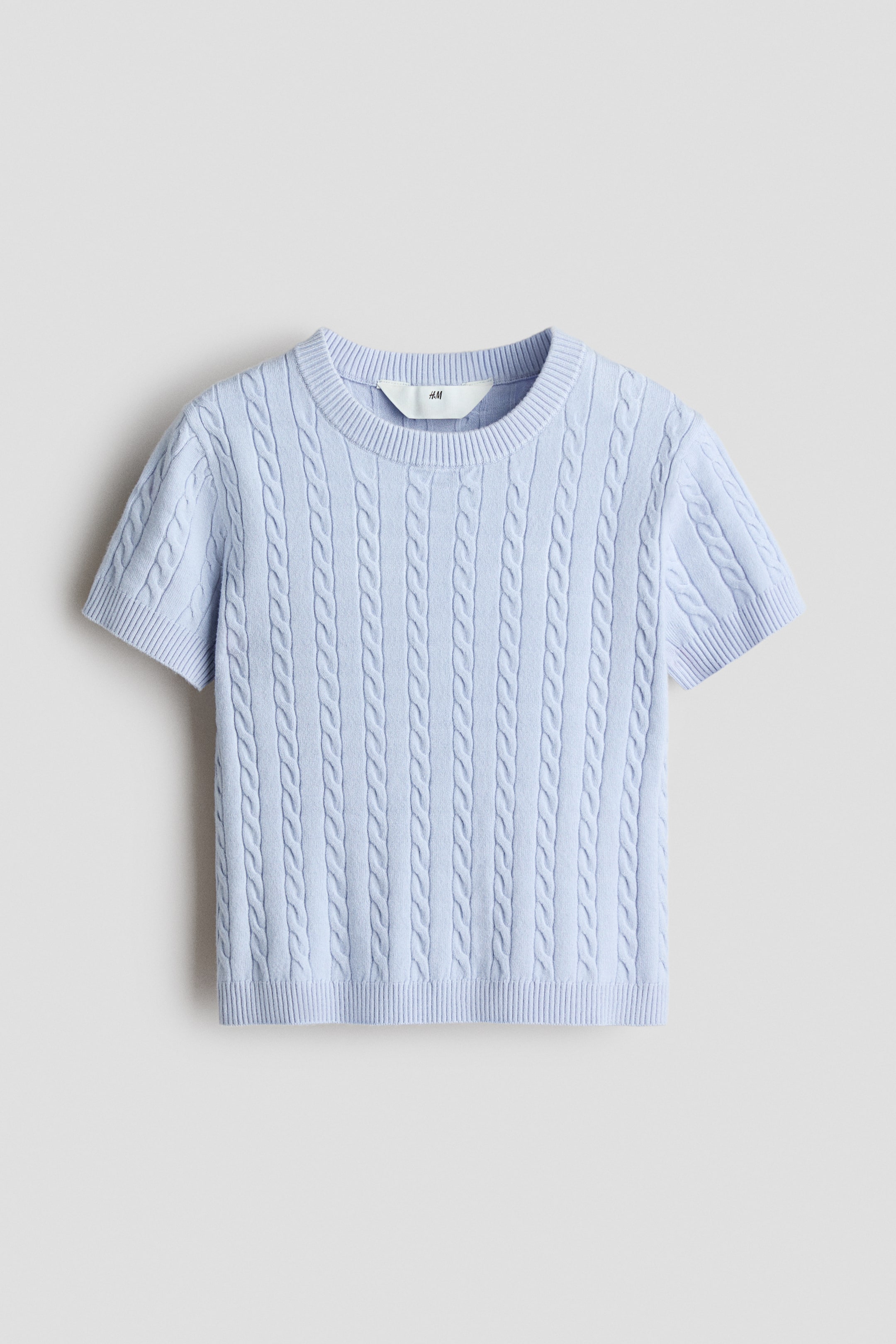 View larger image: A light blue short top showcasing a cable knit pattern, with a round rib-trimmed neckline, short sleeves, and ribbing at the cuffs and hem. The top is laid flat, facing forward.