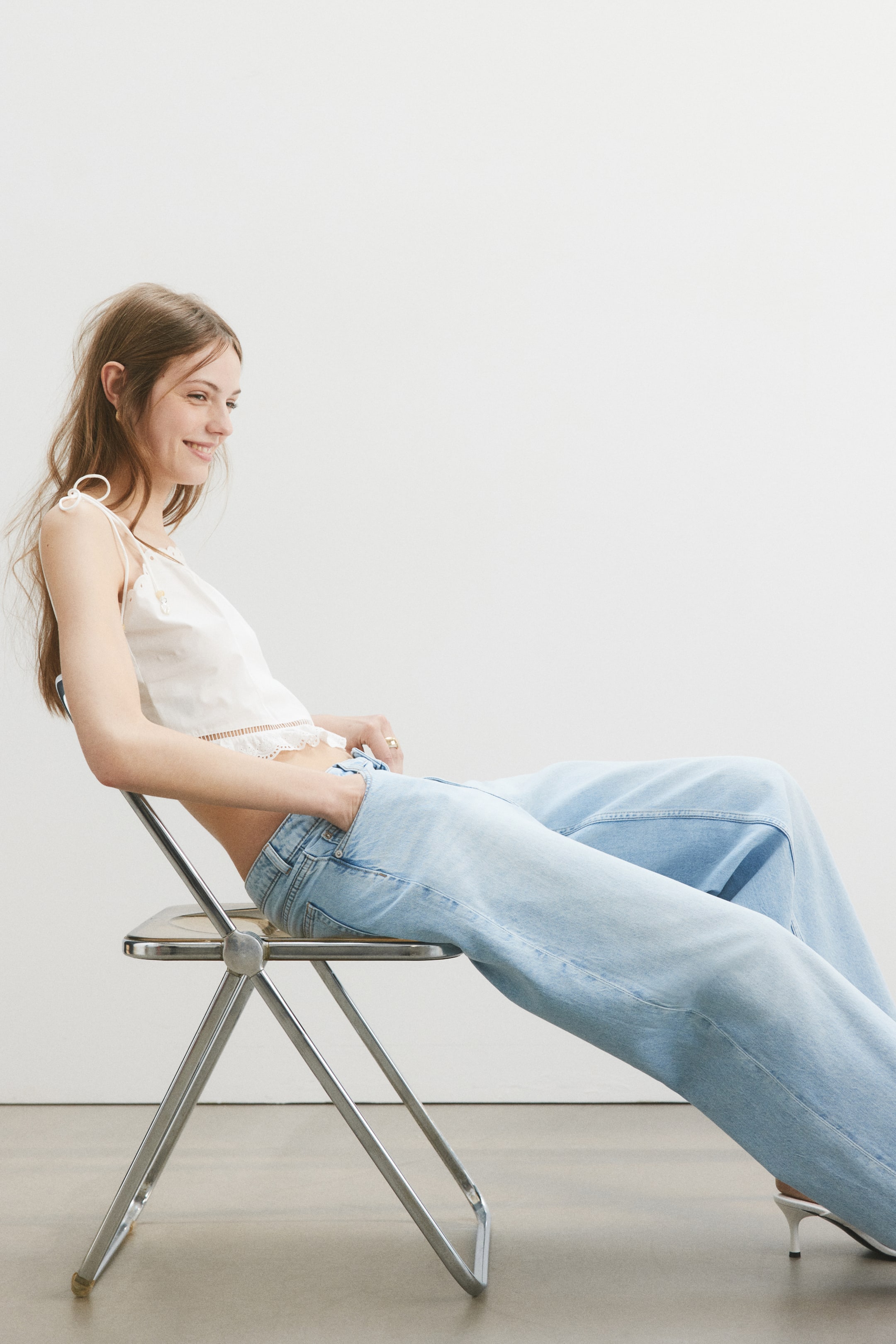 Visa större bild: En vit kort topp med knytband på axlarna, prickigt mönster och en vågig broderad kant längs fållen, bärs tillsammans med ljusblå, högmidjade, vida jeans, med båda plaggen vinklade åt vänster.