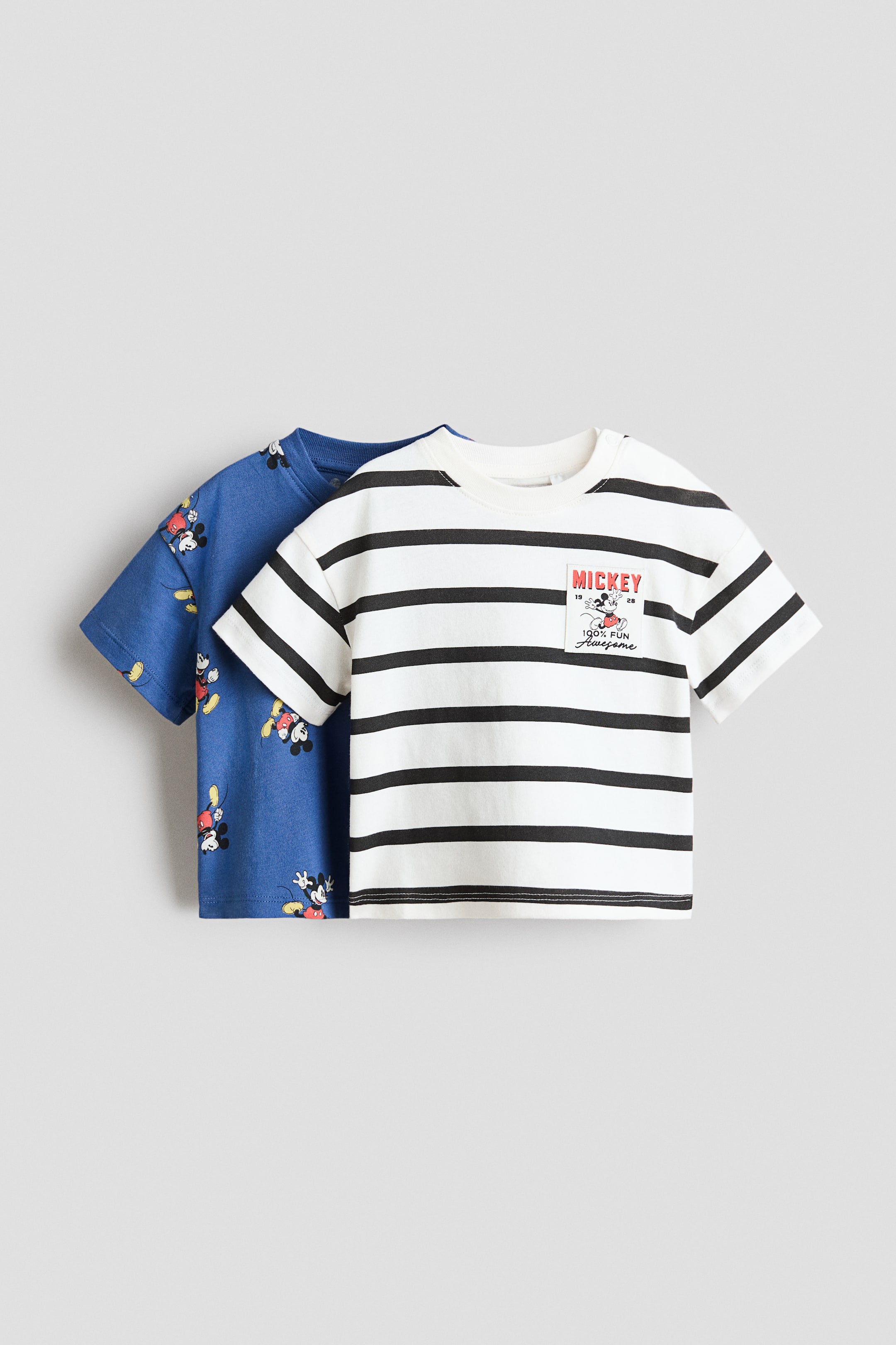 View larger image: Presenting a 2-pack of short-sleeved, crew neck T-shirts: The first T-shirt is white with black horizontal stripes and showcases a front graphic print featuring "MICKEY" in red, "1928", "2023", and "100% FUN Awesome" along with a Mickey Mouse illustration. The second T-shirt, seen at the back, is blue with an all-over print of Mickey Mouse characters.