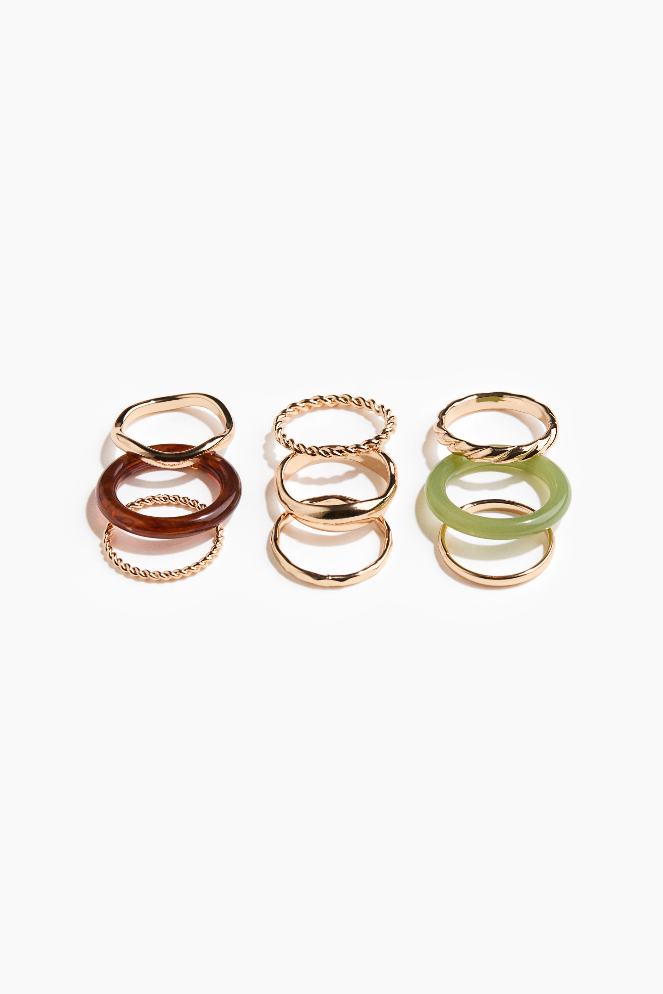 View larger image: A collection of gold-toned and resin rings is arranged in three distinct stacks. Each stack features a combination of slim gold-toned rings with twisted, wavy, or hammered textures, and wider, smooth rings that are either gold-toned, transparent brown resin, or transparent light green resin.