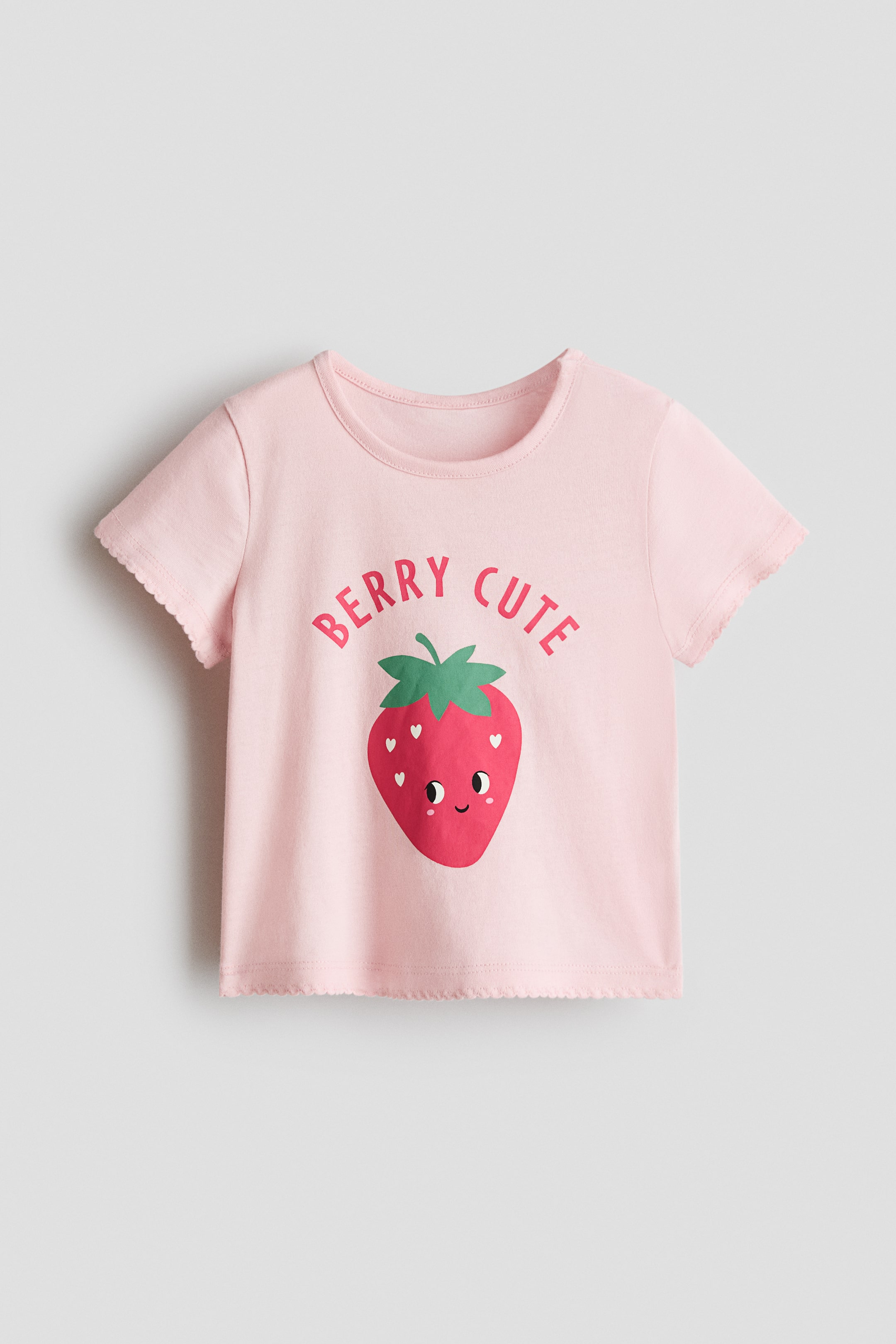 查看大圖: 粉紅色印花棉質上衣,圓領設計,短袖,袖口和下擺均飾有波浪邊。正面展示了一個大大的微笑草莓圖案,上方拱形排列著 "BERRY CUTE" 字樣。