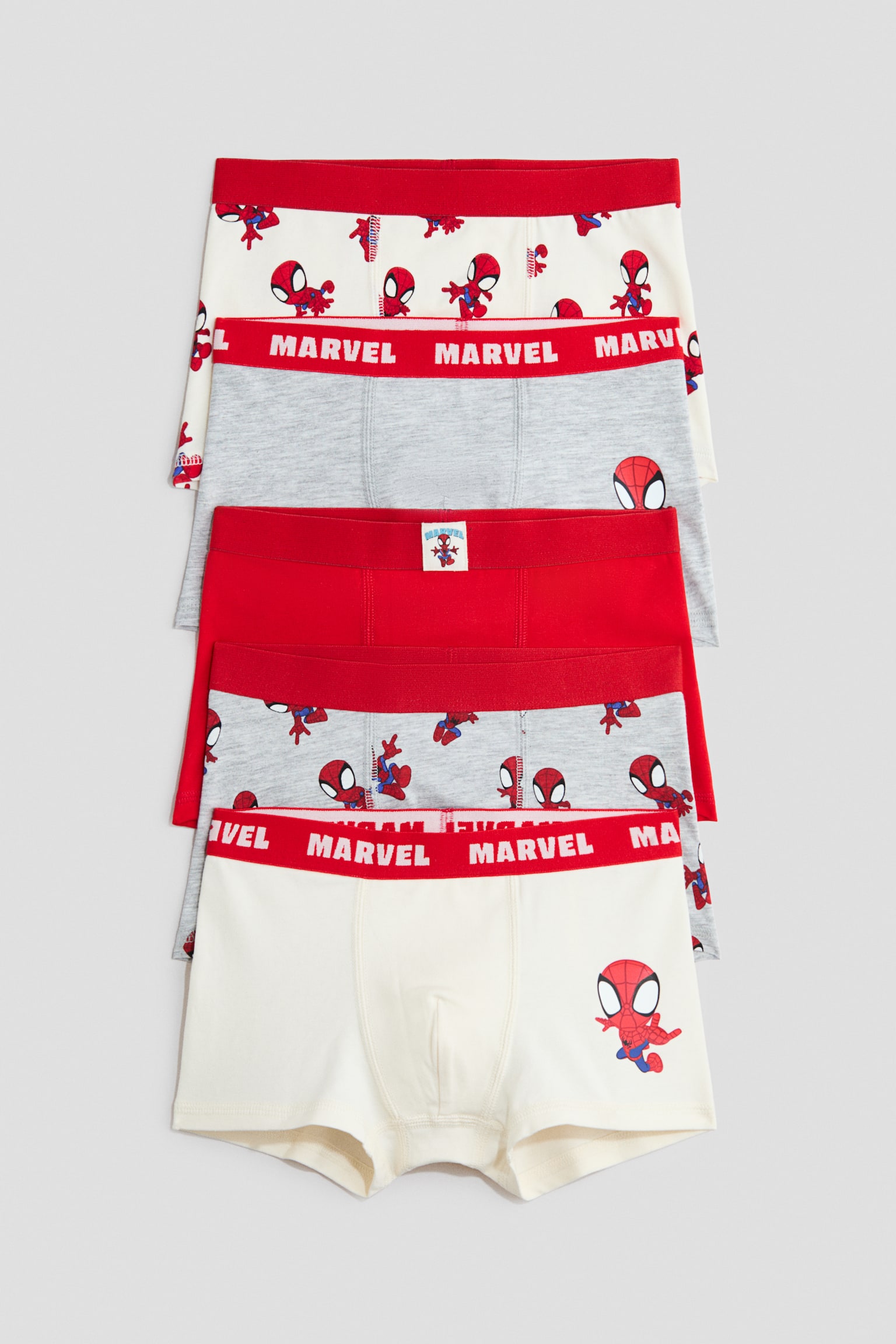 Five cotton jersey boxer briefs are stacked vertically, showcasing their front designs with short legs and elasticated red waistbands. The assortment includes solid red, grey, and off-white styles decorated with Spider-Man graphics and "MARVEL" text on the waistbands.