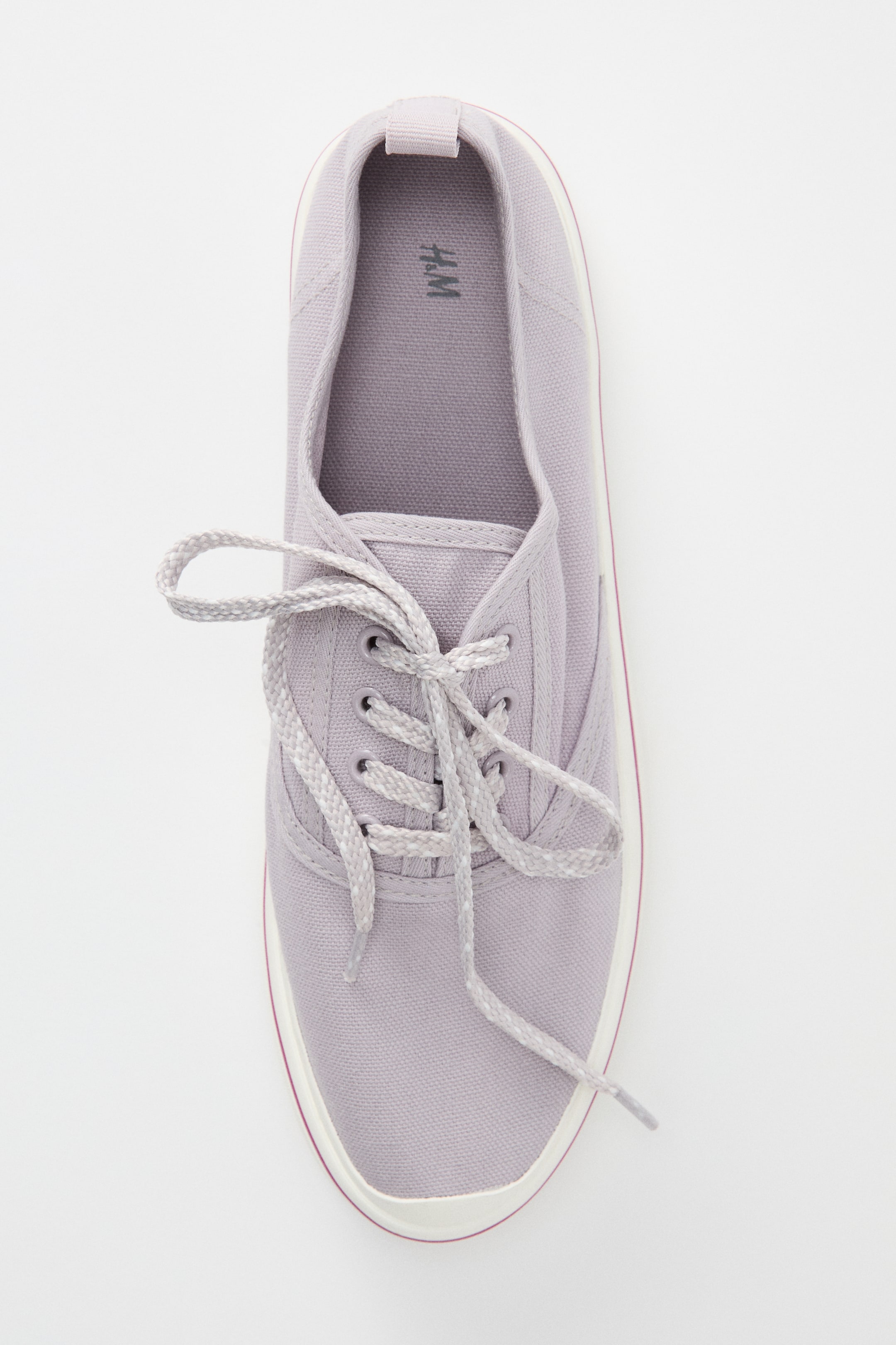 Größeres Bild anzeigen: Ein hellvioletter Baumwoll-Canvas-Sneaker erscheint aus der Vogelperspektive, mit einer vorne zu einer Schleife gebundenen Schnürung, einer Stoffschlaufe an der hinteren Öffnung und einem Baumwoll-Canvas-Futter, alles umrahmt von einer weißen Gummisohle mit einem dünnen roten Streifen.