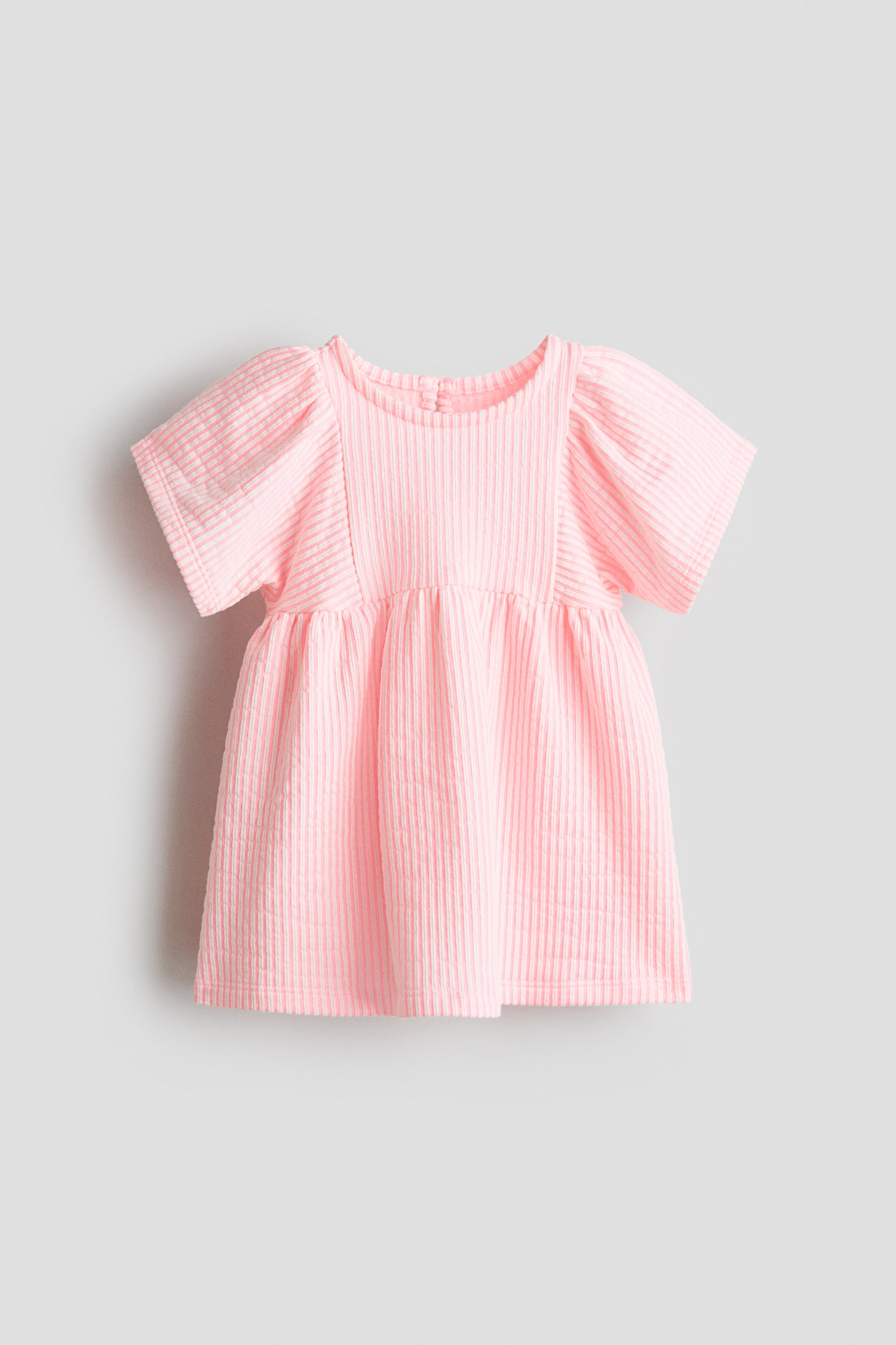 View larger image: A pink dress shown from the front, featuring a finely ribbed texture, a round neckline with a keyhole opening fastened by a button at the back, and short puffed sleeves. Gathers form at the waist, leading to a flared skirt.