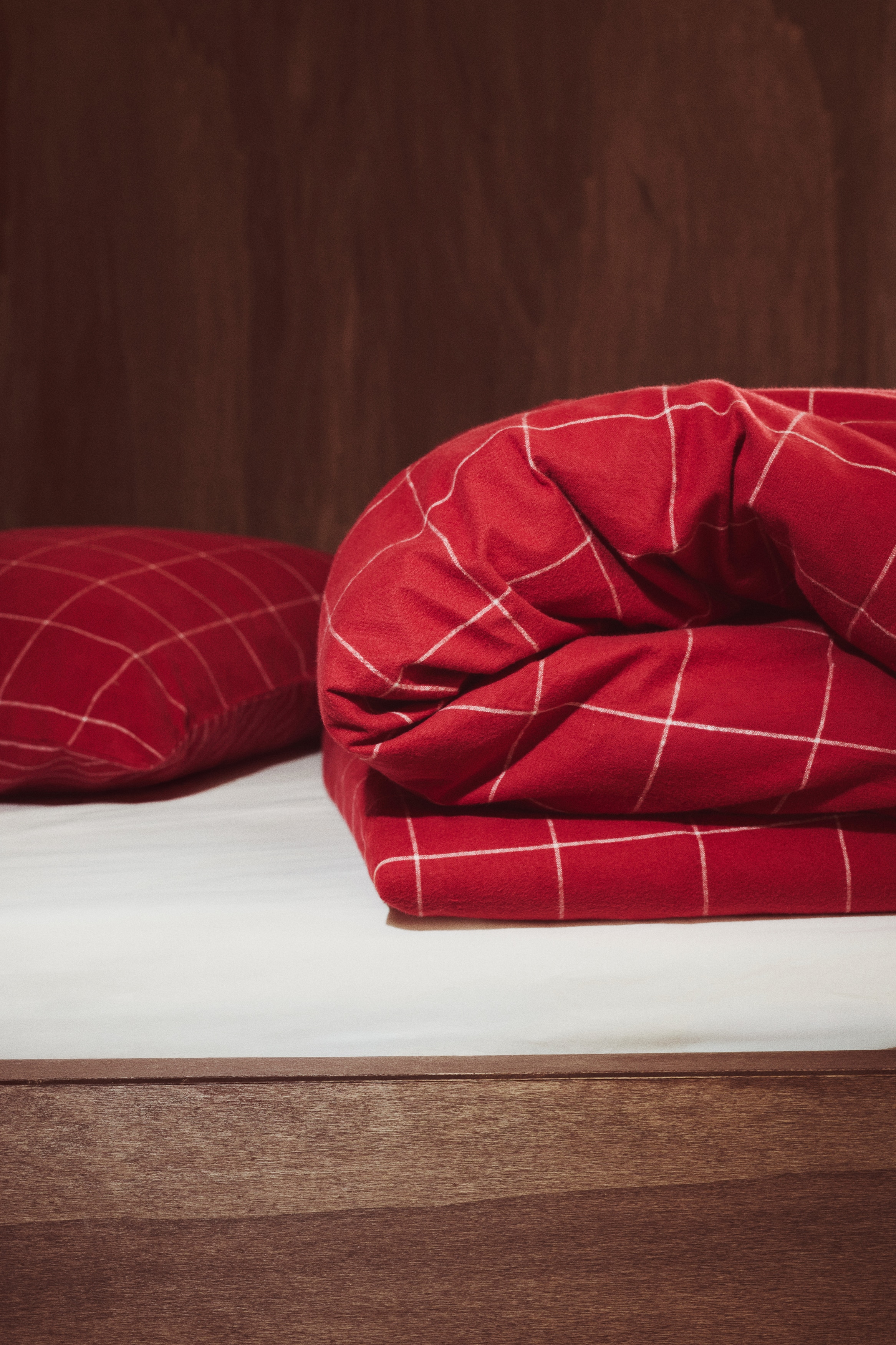 A single quilt cover set made of red cotton flannel featuring a white grid pattern is resting in a folded stack, facing front. The set includes a matching rectangular pillowcase sitting on top of the neatly folded quilt cover.