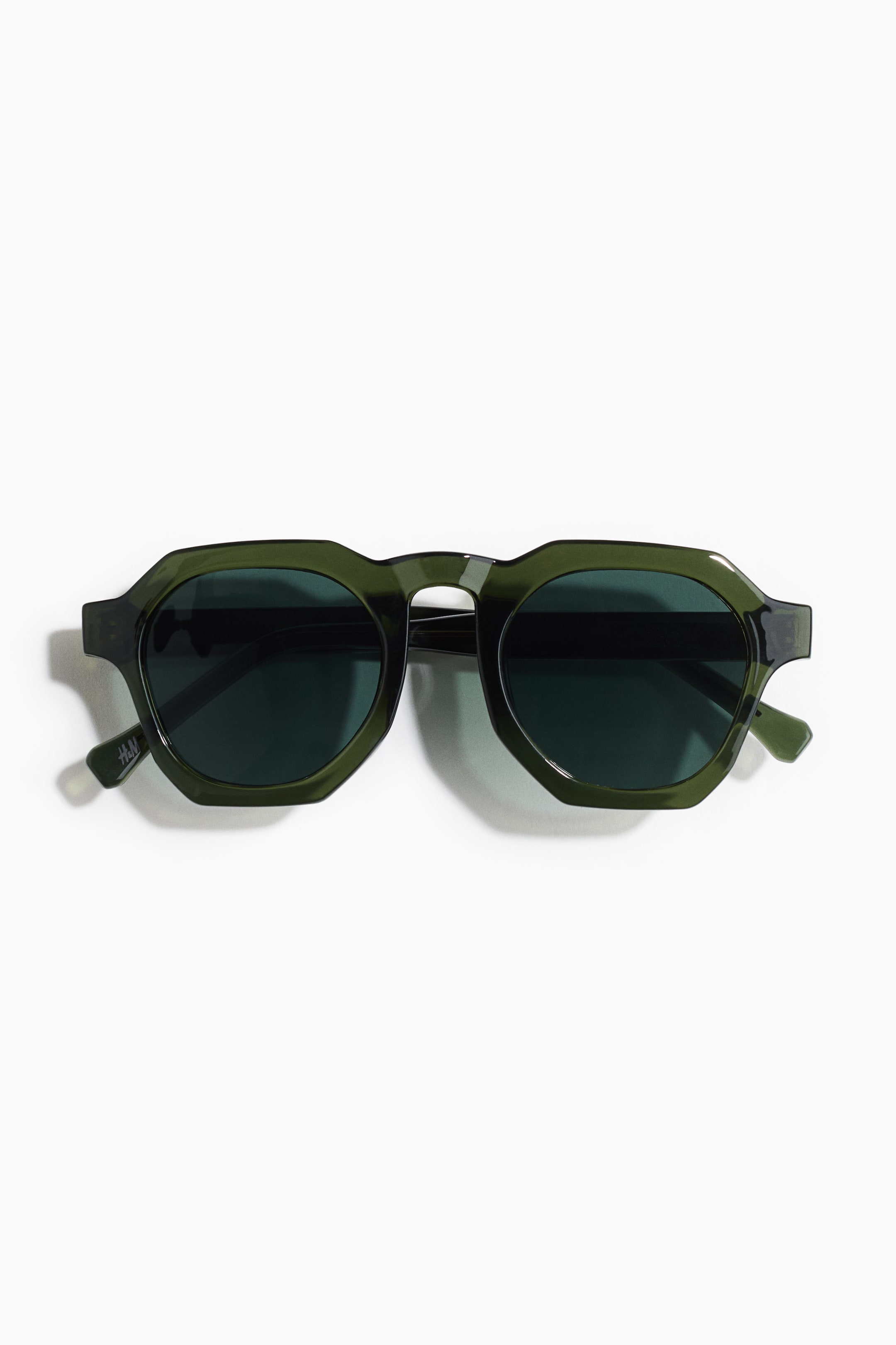 View larger image: Hexagon-shaped sunglasses are showcased in a front view, featuring dark green plastic frames along with matching side pieces. They come equipped with dark, tinted plastic lenses.