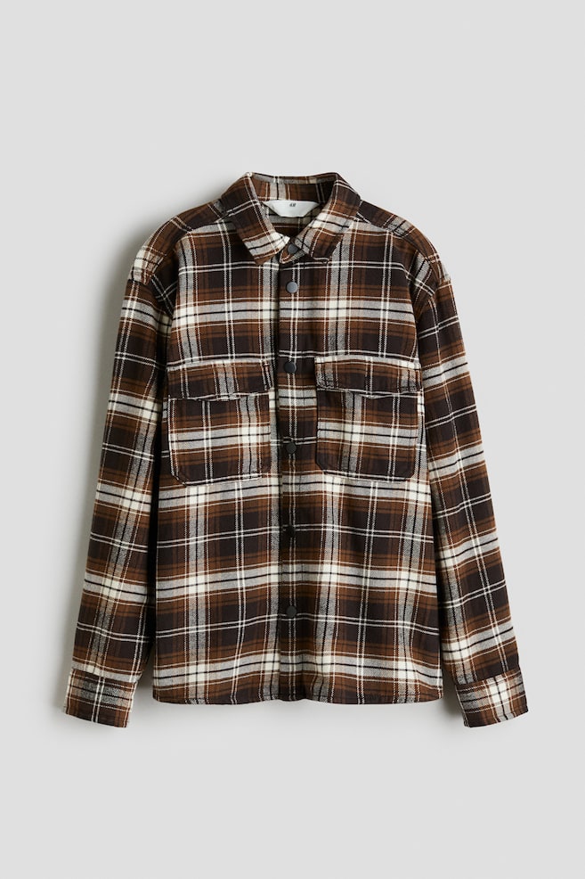 Una camicia a quadri marrone, nera e bianca è mostrata dal davanti, con un colletto standard, una chiusura frontale con bottoni a pressione e due tasche sul petto con patta e bottoni a pressione. - 1