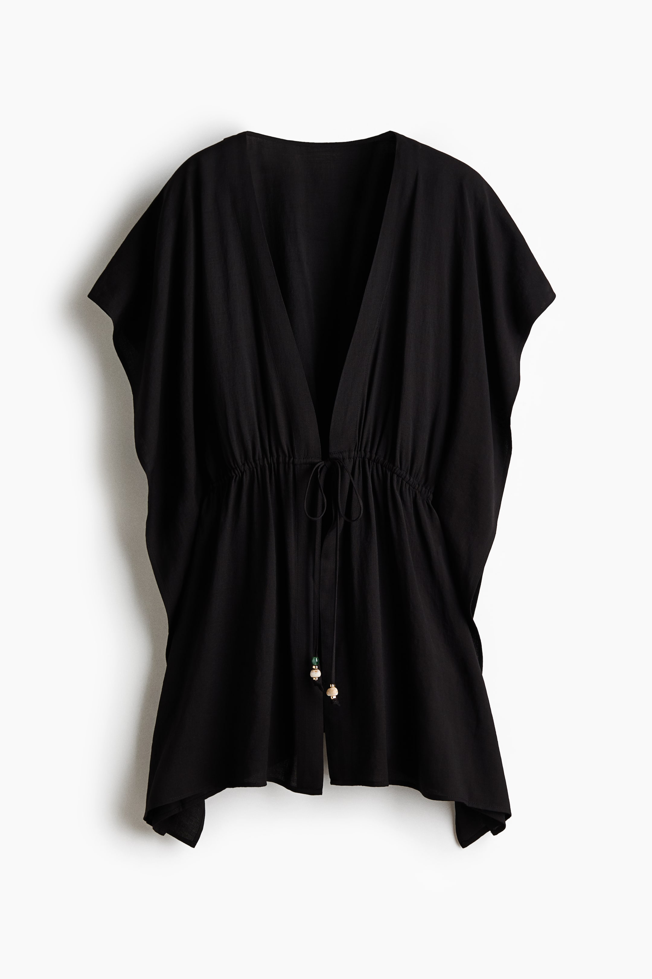 Vezi imaginea mai mare: O rochie kaftan de plajă neagră, scurtă și supradimensionată, este prezentată din față, având un decolteu adânc în V, mâneci scurte și un șnur care strânge talia, ale cărui capete sunt împodobite cu mărgele decorative.