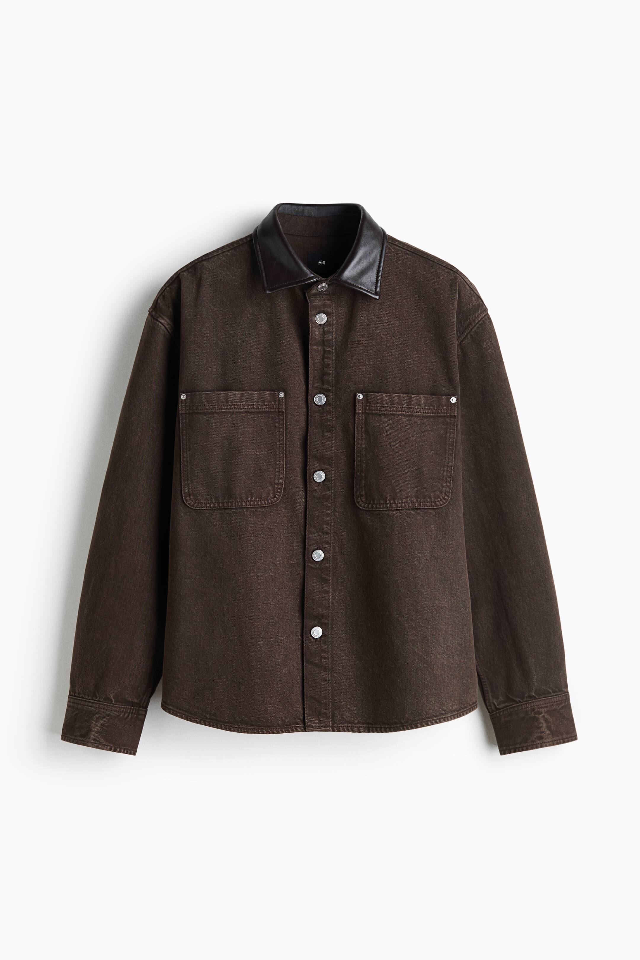 View larger image: A dark brown denim shirt-jacket is shown from the front, featuring a contrasting black leather-look collar and a silver button-down front closure. The jacket includes two large chest patch pockets with silver rivet details and long sleeves with buttoned cuffs.