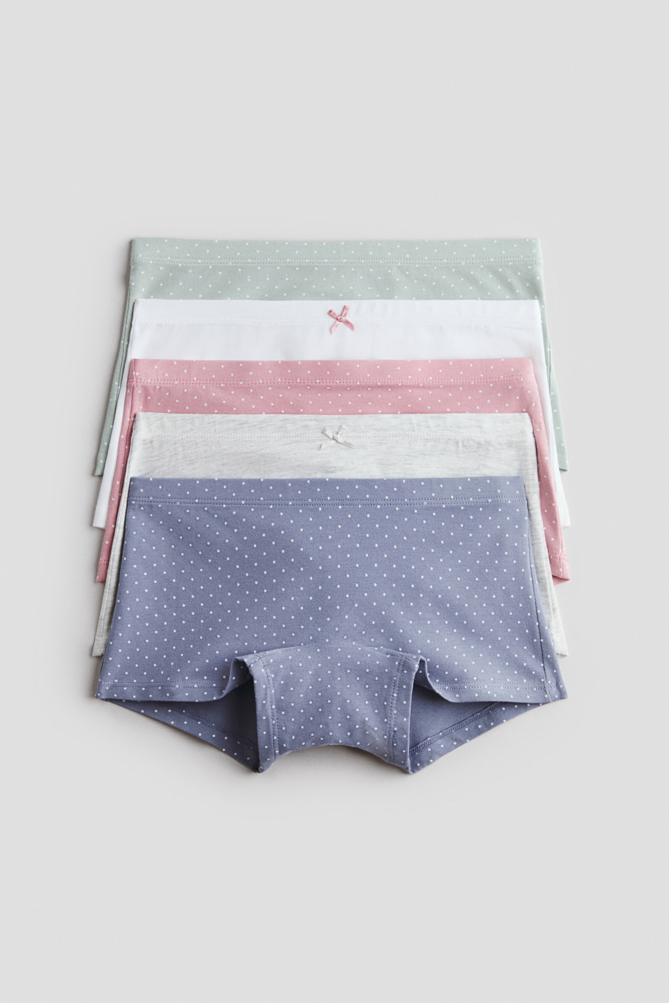 Visualizza immagine più grande: Cinque paia di boy shorts sono impilati, con il paio anteriore blu caratterizzato da pois bianchi e che mostra le aperture delle gambe. Quattro paia aggiuntive sono stratificate dietro di esso, mostrando le loro cinture in grigio chiaro, rosa con pois bianchi, bianco e verde chiaro con pois bianchi, con piccoli fiocchi visibili sulle cinture rosa, bianca e grigia.