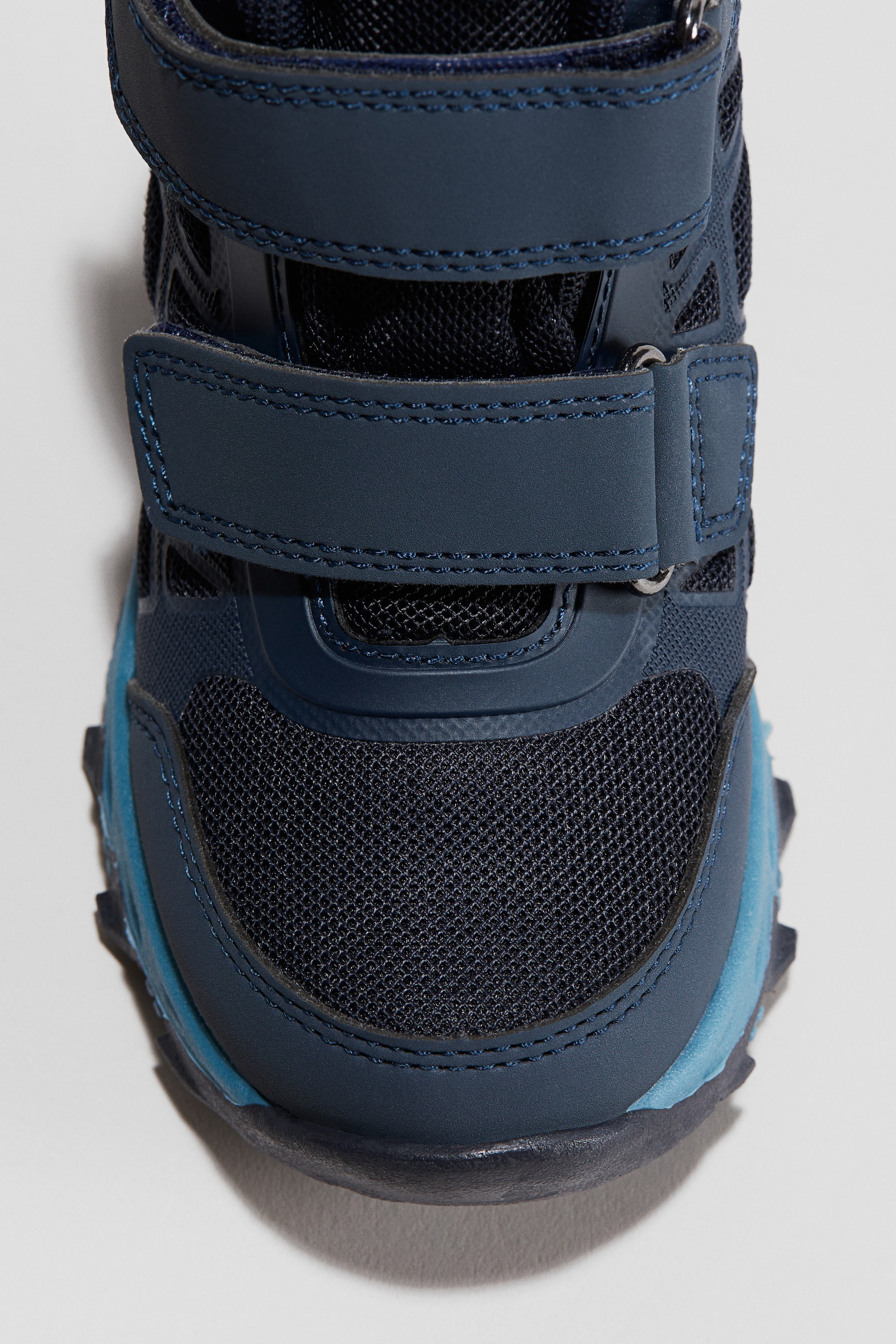 Visa större bild: Trackmid Wp 2v Supportive, funktionella barnstövlar presenteras framifrån, med en marinblå ovandel konstruerad med mesh och syntetiska överlägg. Två marinblå kardborreband fäster över mellanfoten, och en ljusare blå accent pryder sidan av tån och mellansulan.