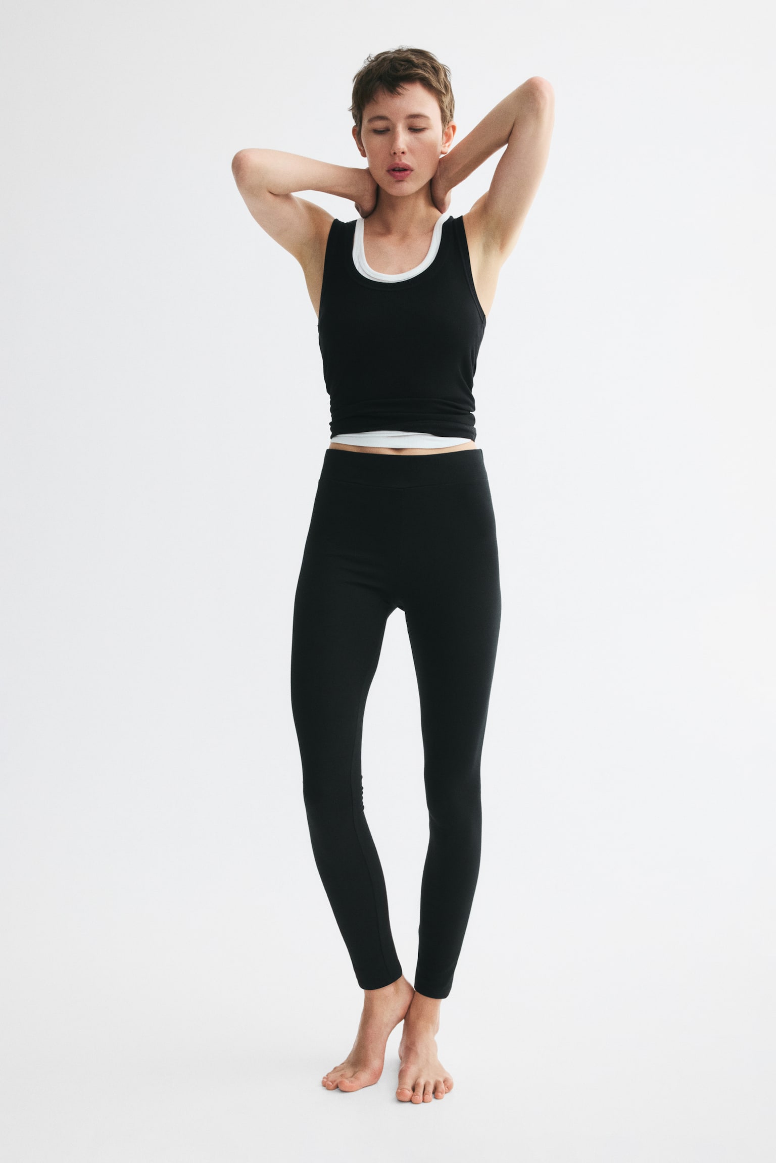 Black leggings are presented flat, featuring a wide, flat waistband and tapering, ankle-length legs. The front view highlights their fitted design. - 1