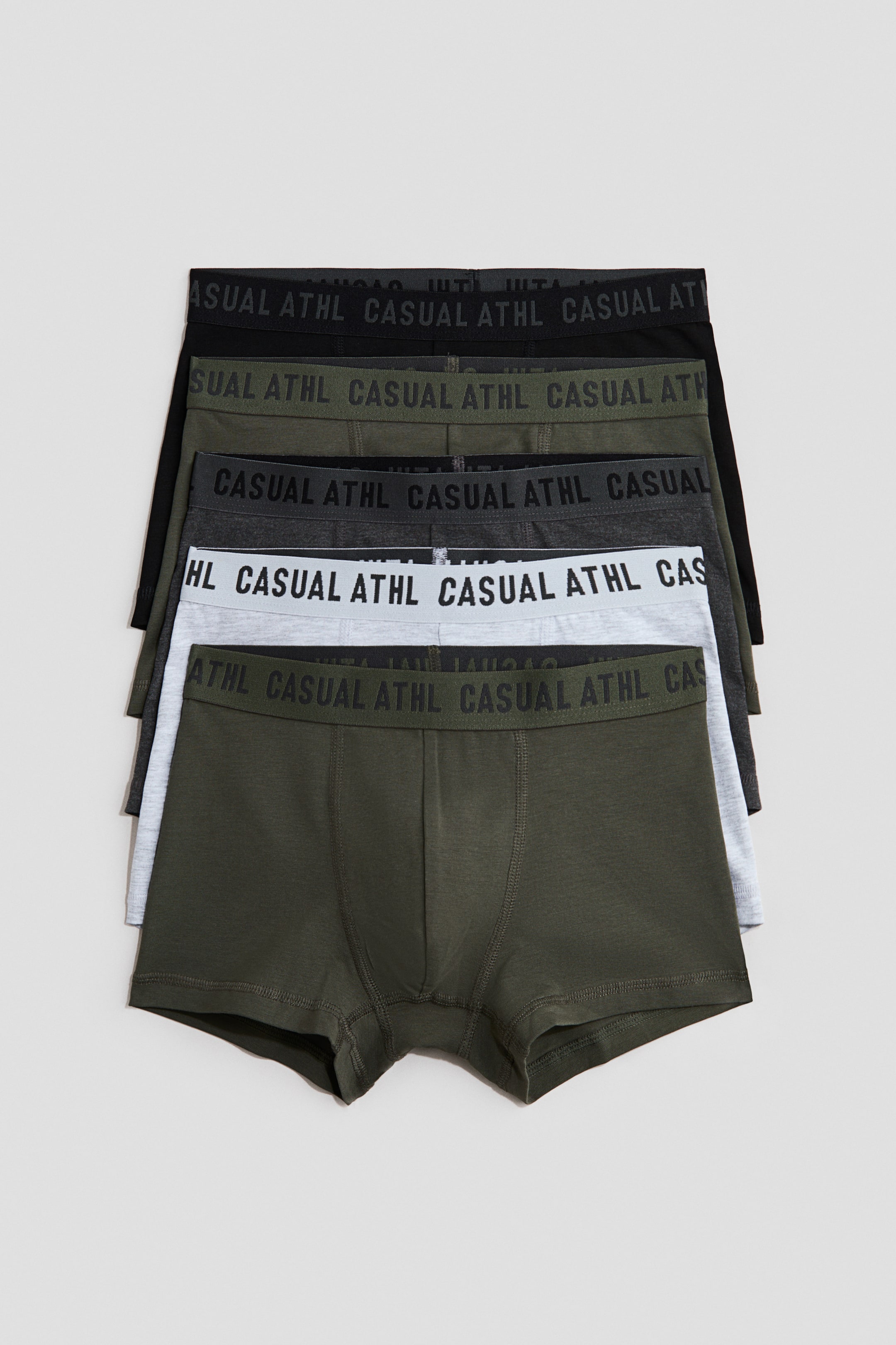 View larger image: A stack of five pairs of cotton jersey trunks is visible, showcasing short legs, an elasticated waist, and a lined front. The trunks are available in shades of olive green, light grey, dark grey, and black, with each elasticated waistband featuring the text "CASUAL ATHL".