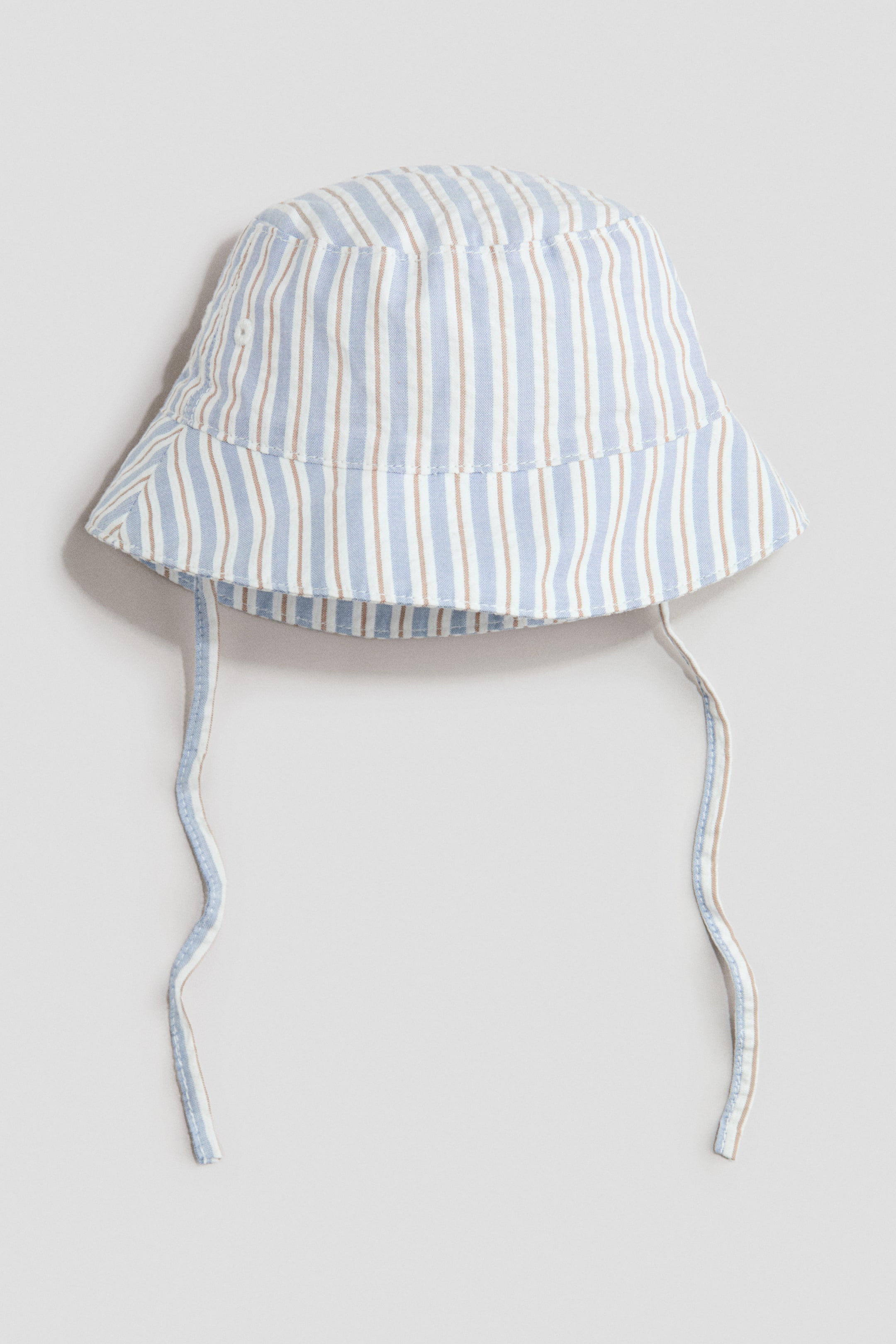 View larger image: The sun hat is showcased from the front, highlighting a gentle weave and a striped pattern with alternating light blue, white, and light brown vertical lines. It is crafted with a rounded crown, a downturned brim, and two fabric ties hanging from its sides; the hat is lined.