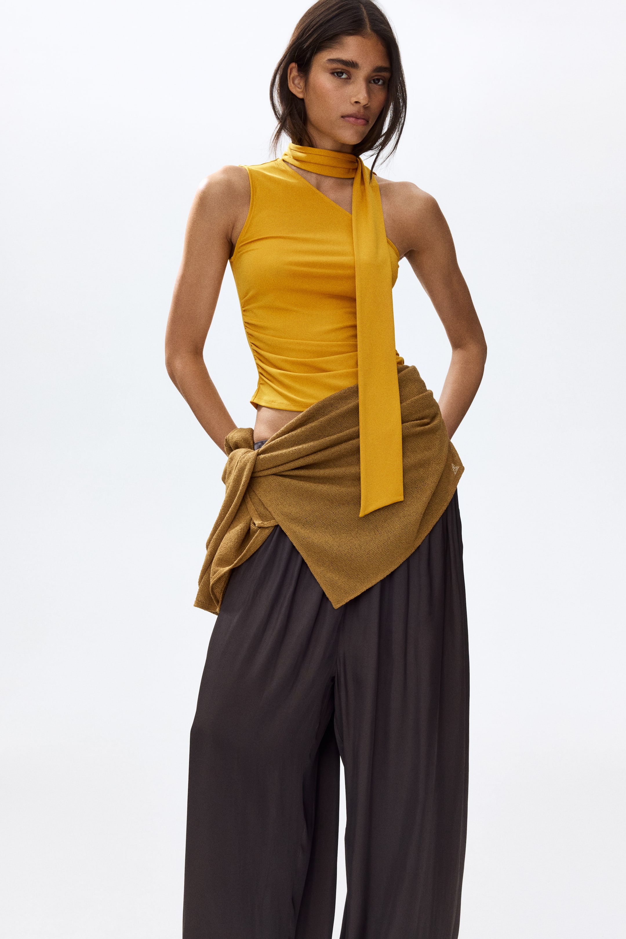View larger image: The model is showcasing a yellow one-shoulder top, featuring an asymmetric design with a broad shoulder strap and a scarf collar elegantly draped around the neck. The gathered side seams lend a softly draped effect to the top.
