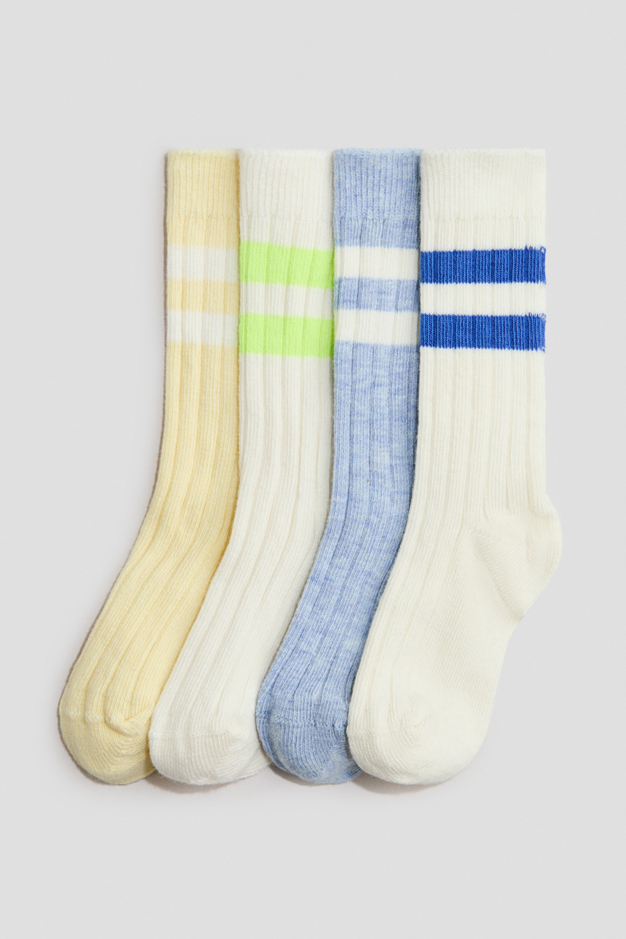 View larger image: H&M Adorables rib-knit socks are presented as a set of four, each sock shown from the front with two horizontal stripes near the cuff. The set features a light yellow sock with white stripes, an off-white sock with neon green stripes, a light blue sock with white stripes, and an off-white sock with blue stripes.