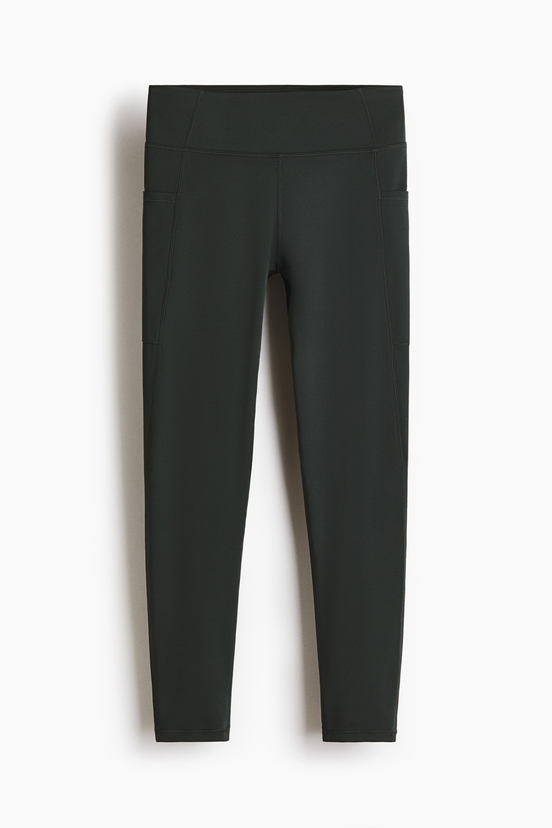 Agrandir l'image: Les leggings de sport vert foncé se présentent en AVANT, avec une ceinture haute et large ainsi que des poches pratiques le long des coutures latérales des deux jambes. Les leggings sont conçus avec une longueur capri.
