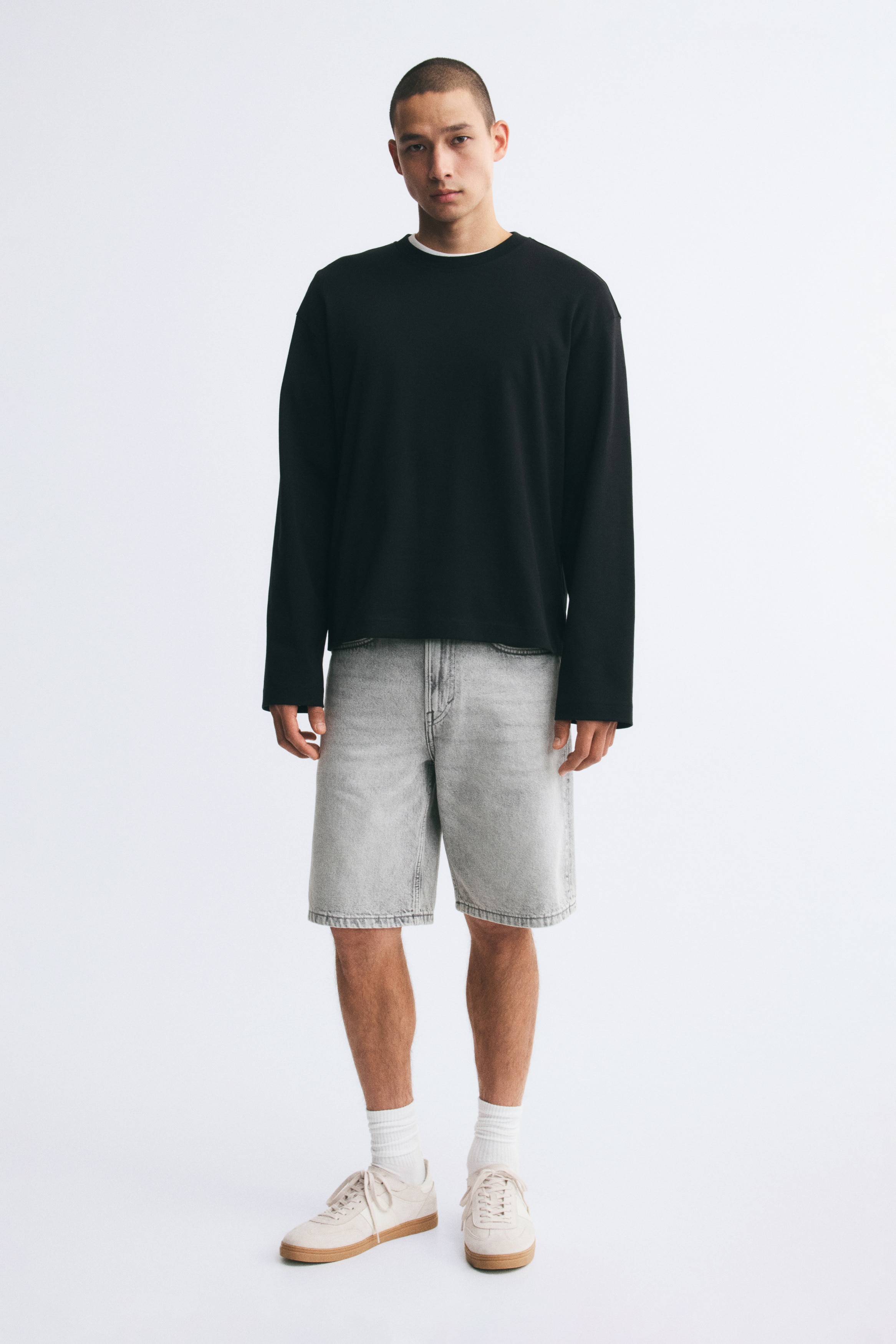 Ein Paar hellgraue Jeansshorts ist von vorne zu sehen, mit einem Fünf-Taschen-Design inklusive einer Münztasche. Es zeigt Gürtelschlaufen und einen Knopfverschluss an der Taille, wobei der Denimstoff eine ausgewaschene Optik aufweist.