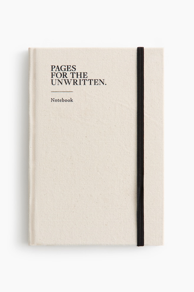 A cream-coloured, fabric-bound notebook is shown facing front, featuring the black-printed text "PAGES FOR THE UNWRITTEN." and "Notebook" on the upper-left cover. A vertical black elastic band runs along the right side of the cover to secure it. - 1