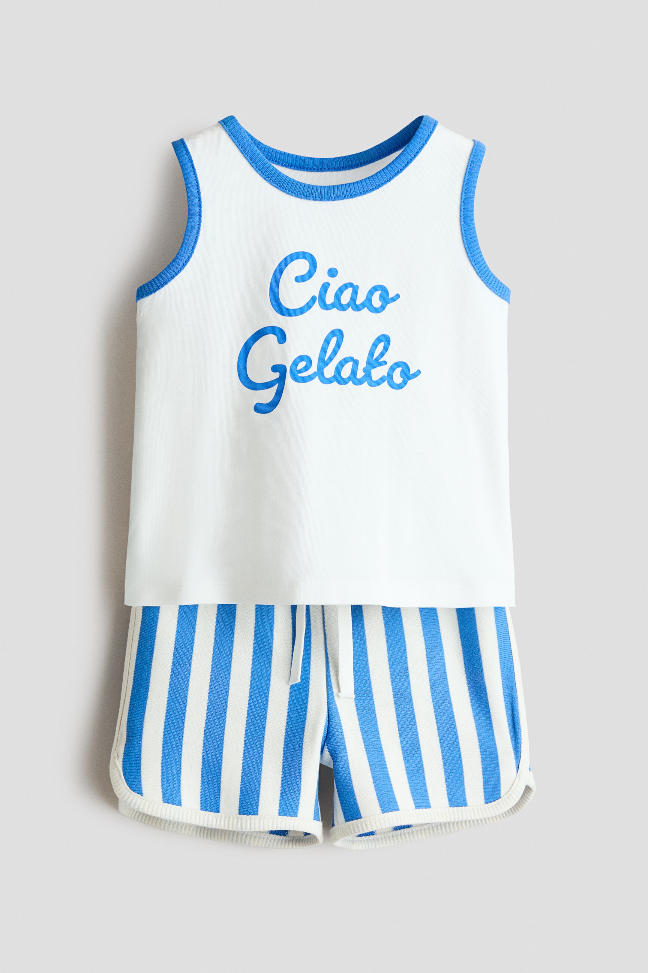 View larger image: A white sleeveless top and blue and white striped shorts form a two-piece set, facing front. The top features blue ribbed trim on the round neckline and armholes, with the text 'Ciao Gelato' in blue on the front. The shorts showcase a white drawstring waist and white ribbed trim along their curved hems.