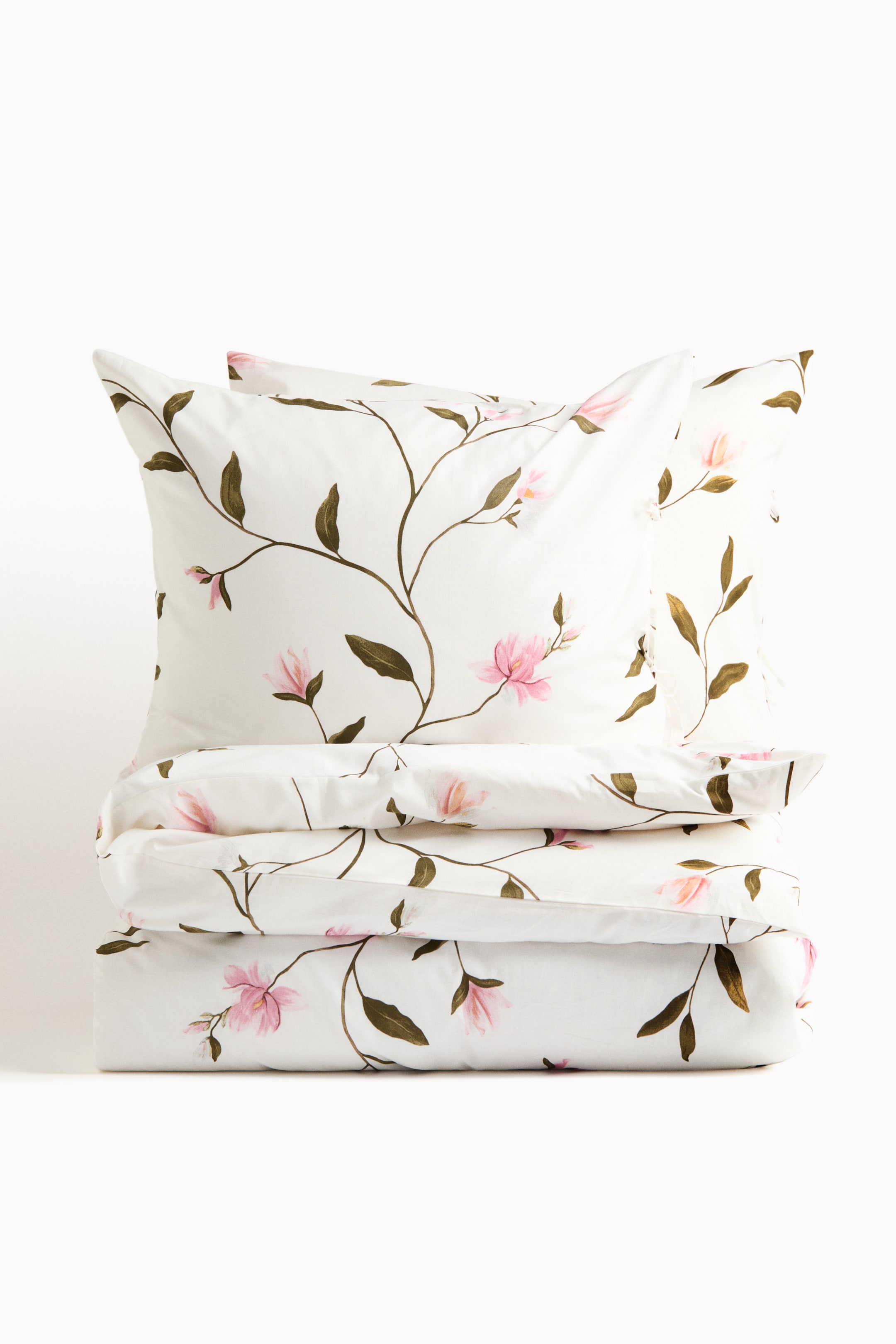 View larger image: A bedding set, consisting of two pillowcases and a folded duvet cover, is displaying a floral pattern on a white base. The pattern is featuring brown-green vines with leaves and soft pink flowers.