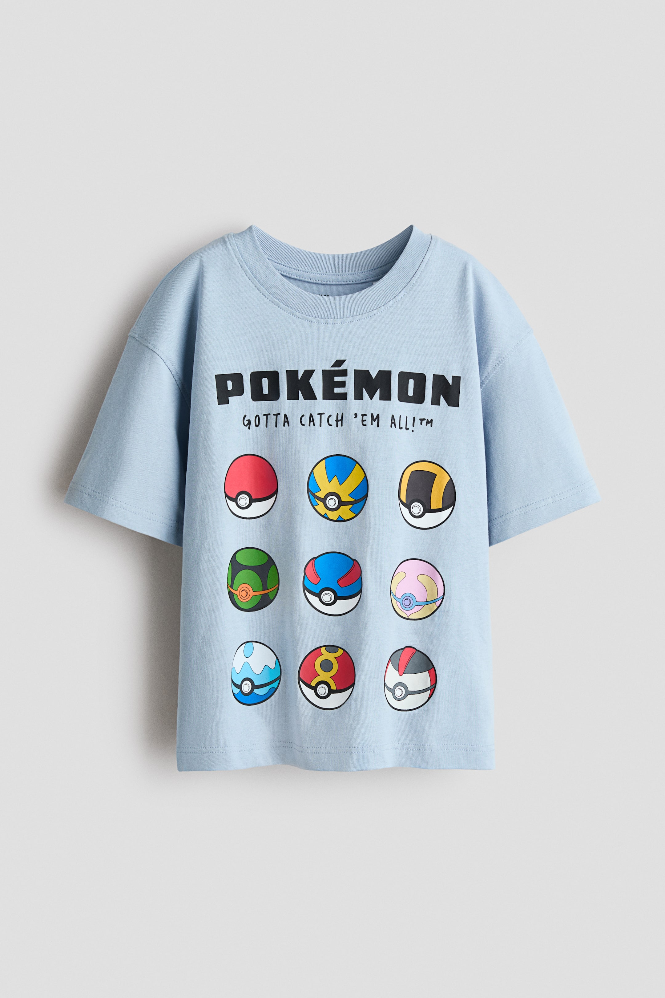 View larger image: The oversized t-shirt showcases its front, crafted from soft, light blue cotton jersey, featuring a ribbed neckline and dropped shoulders. It displays a black "POKÉMON" logo with "GOTTA CATCH 'EM ALL!?" beneath, and nine unique, vibrant Poké Ball designs are arranged below.