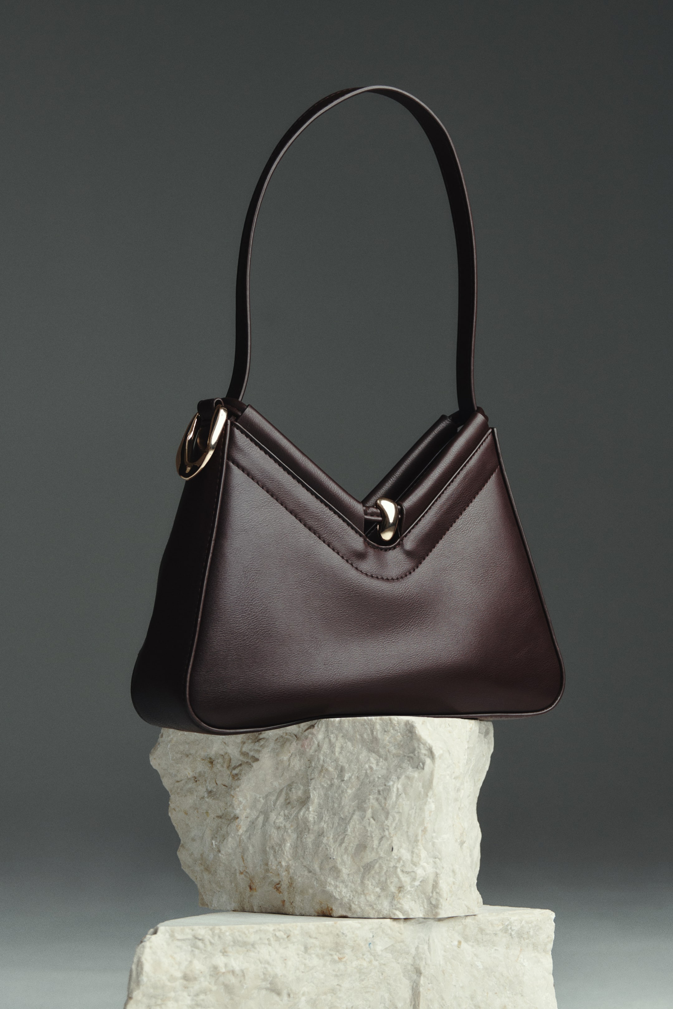 Преглед на по-голямо изображение: Тъмнокафява чанта за рамо от покрит плат, с детайли от златист метал, включително централно магнитно закопчаване на V-образния връх. Късата презрамка е прокарана през златист метален пръстен от едната страна, позволявайки универсален стил.