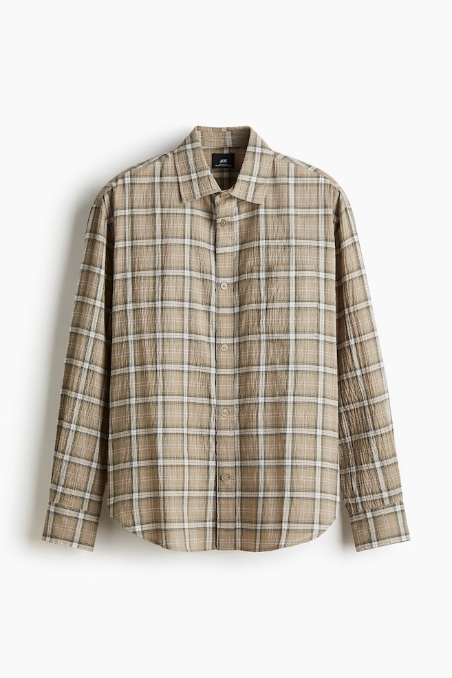 A long-sleeved shirt is displaying its front, featuring a beige, white, and dark brown plaid pattern with a visible crinkled texture. It is showing a standard collar, a full button-front closure, and a rounded hem. - 1