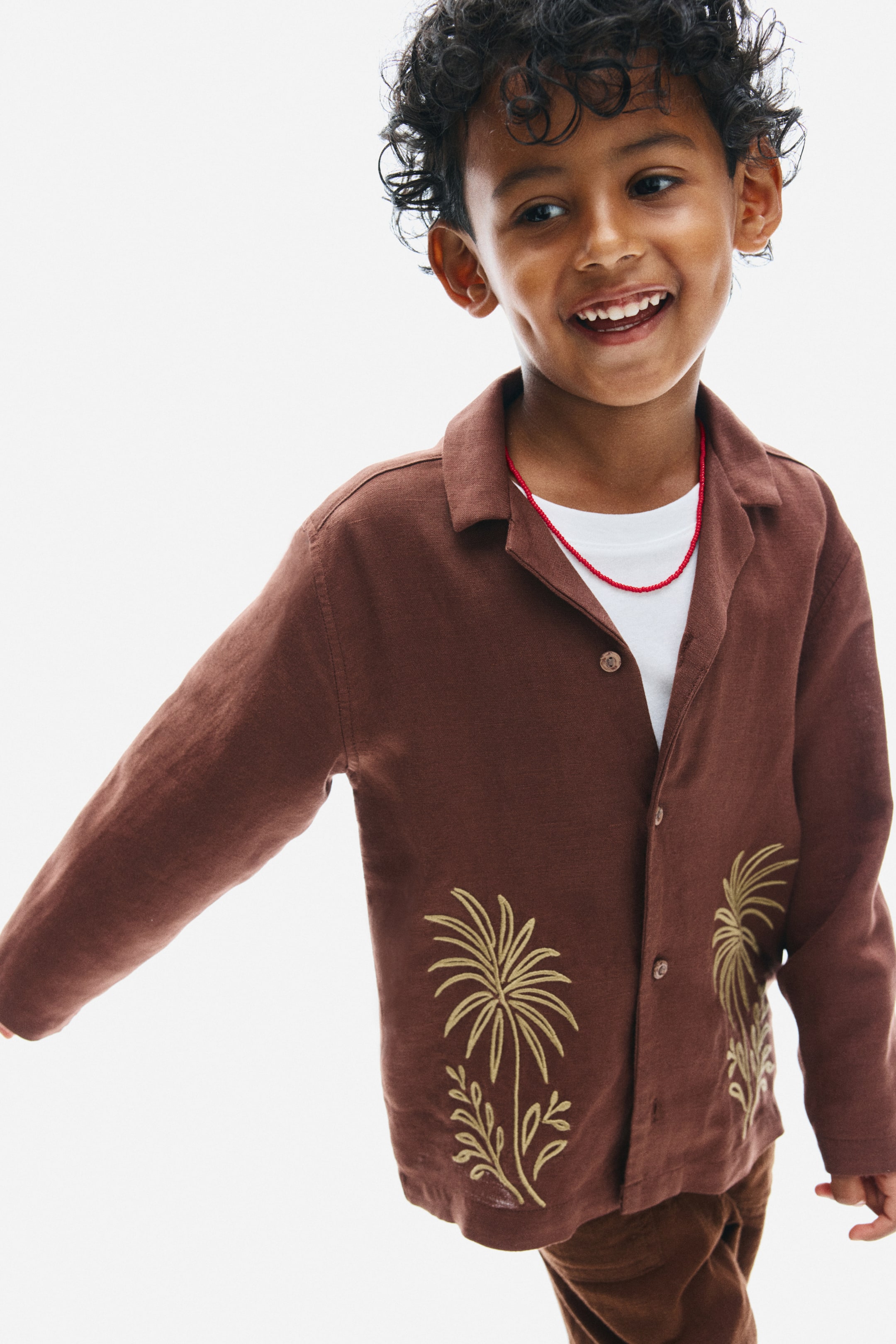 View larger image: A brown long-sleeved shirt in a textured linen-viscose weave is worn front-on, featuring a resort collar and button fastenings. It displays embroidered golden palm tree designs on the lower front panels and is layered over a white T-shirt.