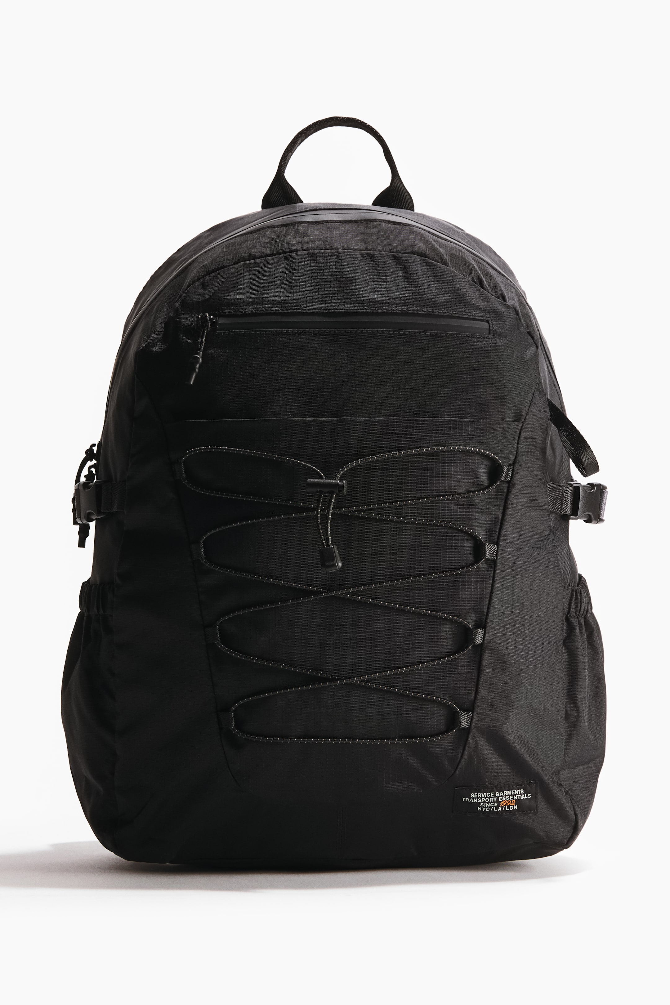 View larger image: A black backpack is facing forward, showcasing a top grab handle and a horizontal zippered front pocket. Criss-crossing bungee cords adorn the lower front, while side compression straps with buckles and elasticated side pockets are visible on the sides.