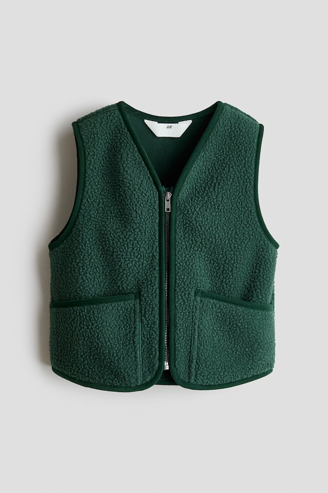 A dark green fleece gilet is showcasing a textured, curly pile fabric, facing front. It features a full-length front zip and two patch pockets on the lower front, all outlined with dark green fabric binding. - 1