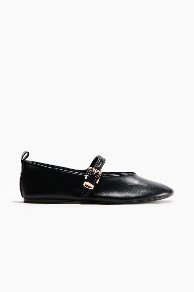 A black Mary Jane flat shoe is featuring a smooth material with a subtly pointed toe. A single strap is securing across the instep with a small, rectangular, gold-toned buckle, and a pull tab is visible at the back heel. - 1
