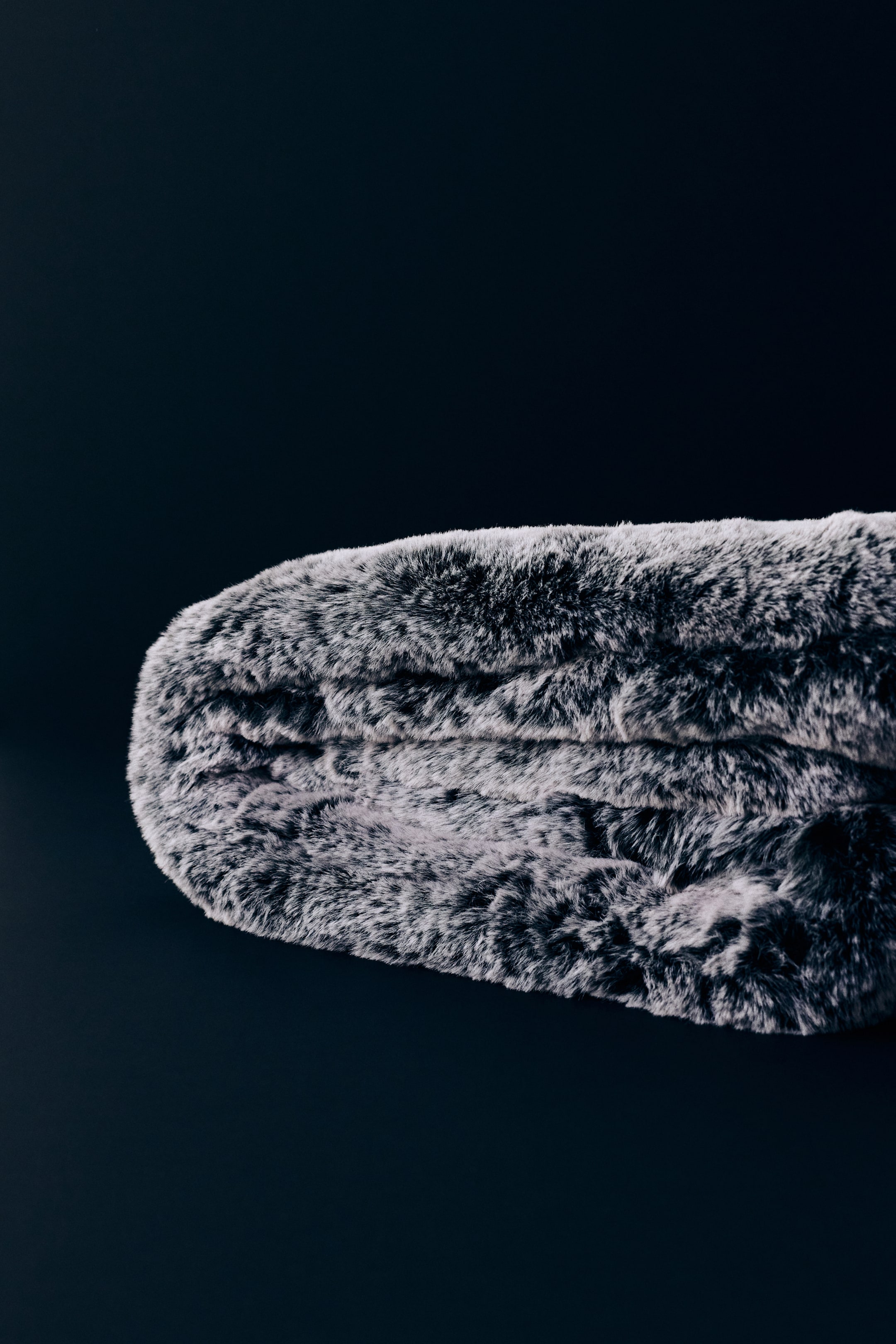 View larger image: A folded throw blanket featuring a super-soft, fluffy fabric is displaying subtly contrasting dark and light tones that create a textured, faux-fur appearance. The thick, plush layers are highlighting the soft volume and dense texture of the throw.