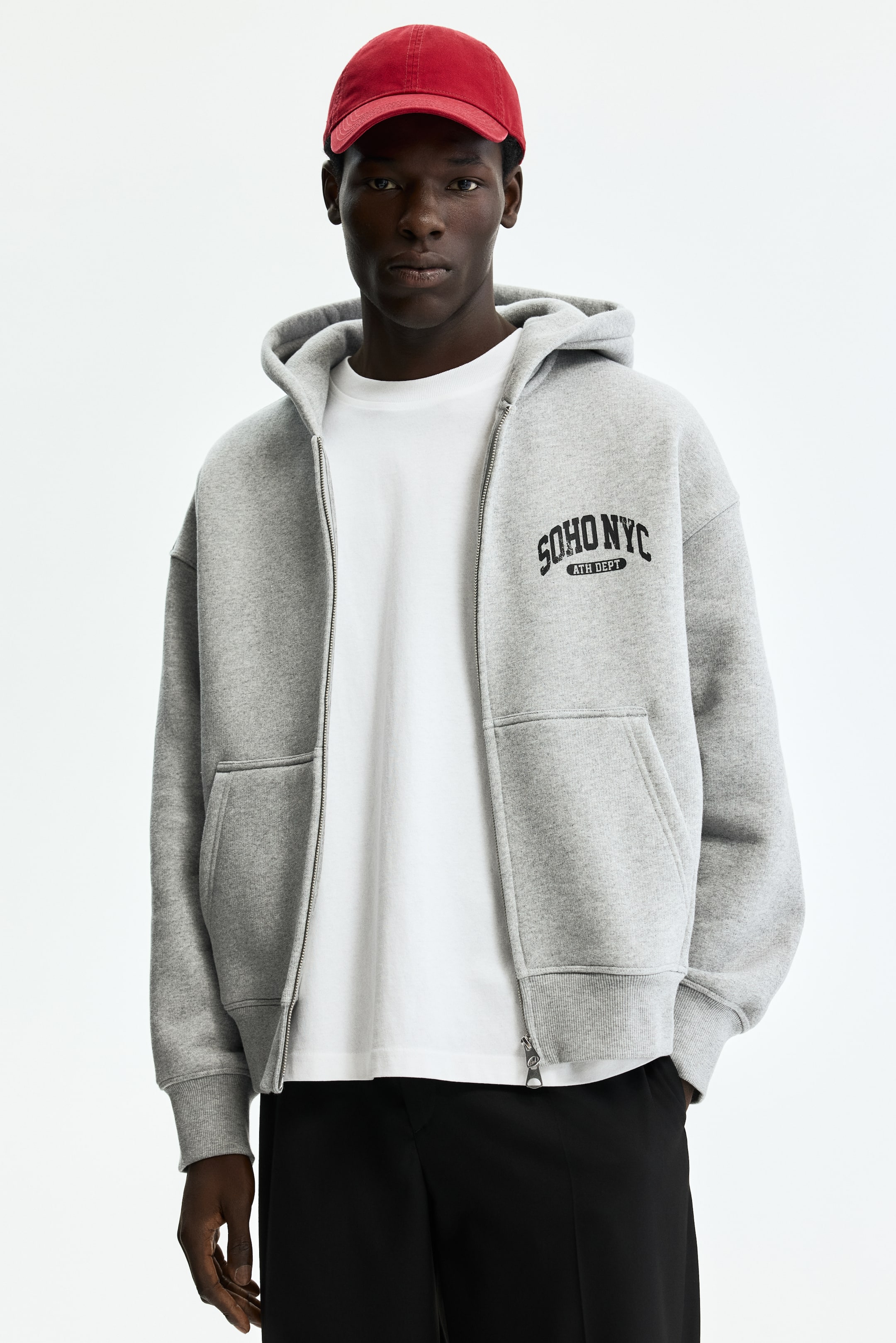 View larger image: A gray zip-up hoodie is showcased, facing forward and open, revealing a white t-shirt underneath. It features a silver-toned front zipper, a hood, front kangaroo pockets, and ribbed cuffs and hem. The left chest displays "SOHO NYC ATH DEPT" printed in black.