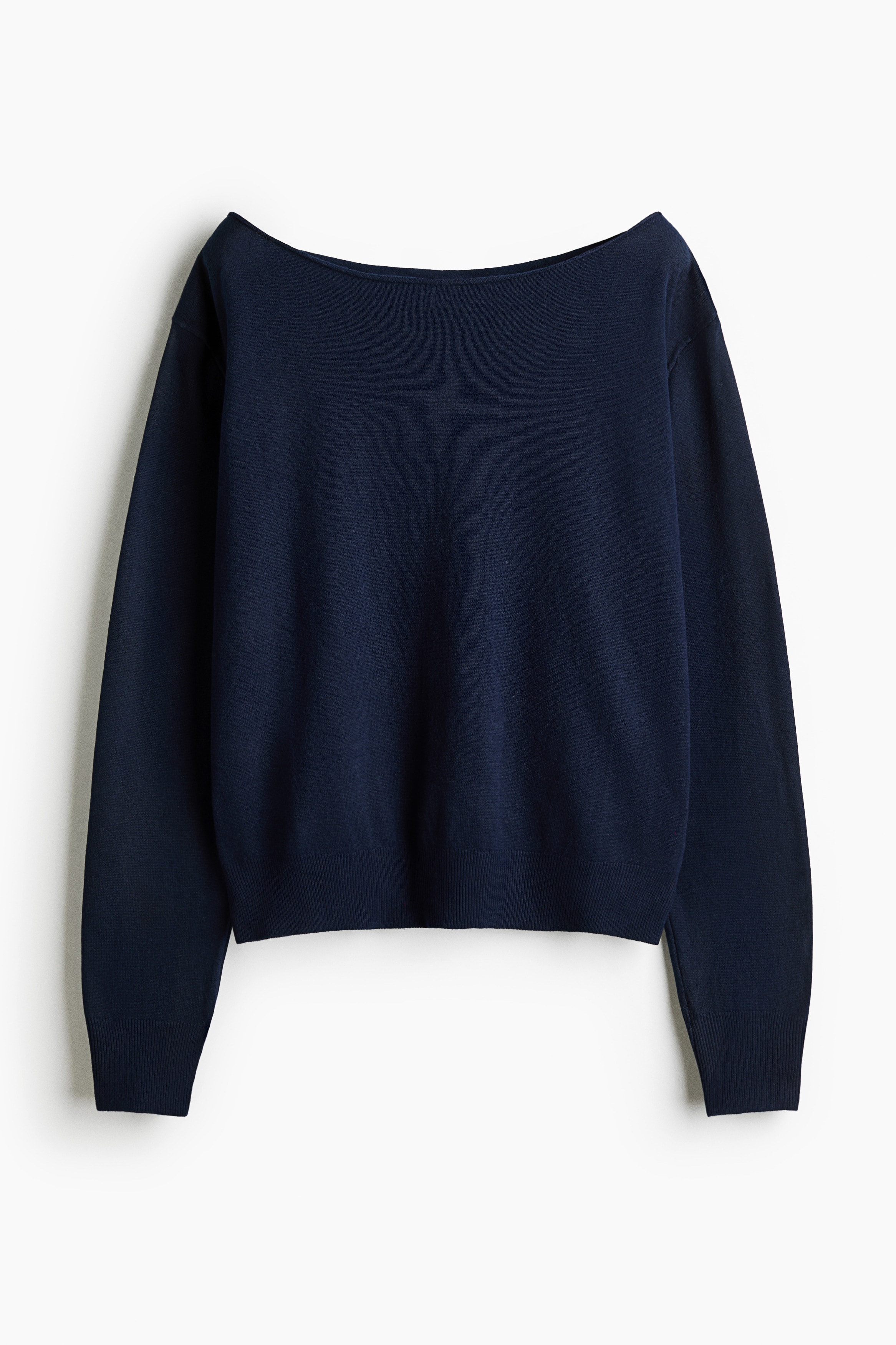A dark blue knit sweater featuring a wide off-the-shoulder neckline, dropped shoulders, and ribbed cuffs is being worn by the model. The sweater is styled with wide-leg, light-wash denim jeans and a black belt, with the model resting one hand against their neck.