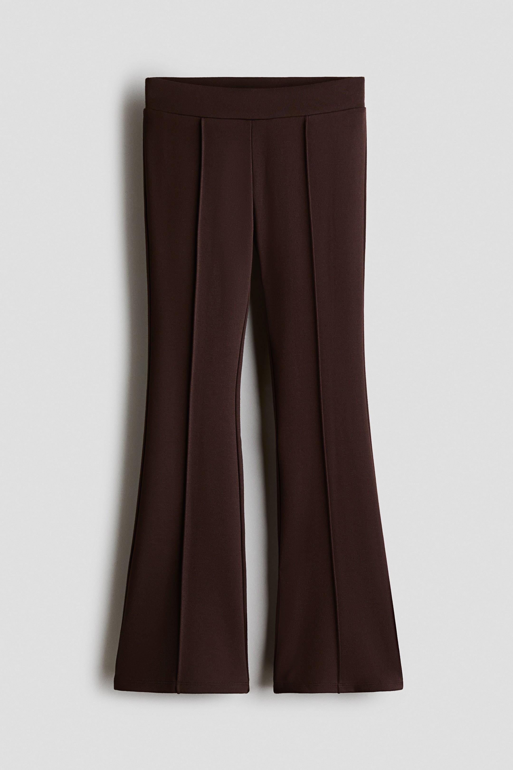 View larger image: Brown flared trousers are shown from the front, featuring a smooth, wide waistband. Vertical stitched creases run down the centre of each leg, which flares out towards the hem.