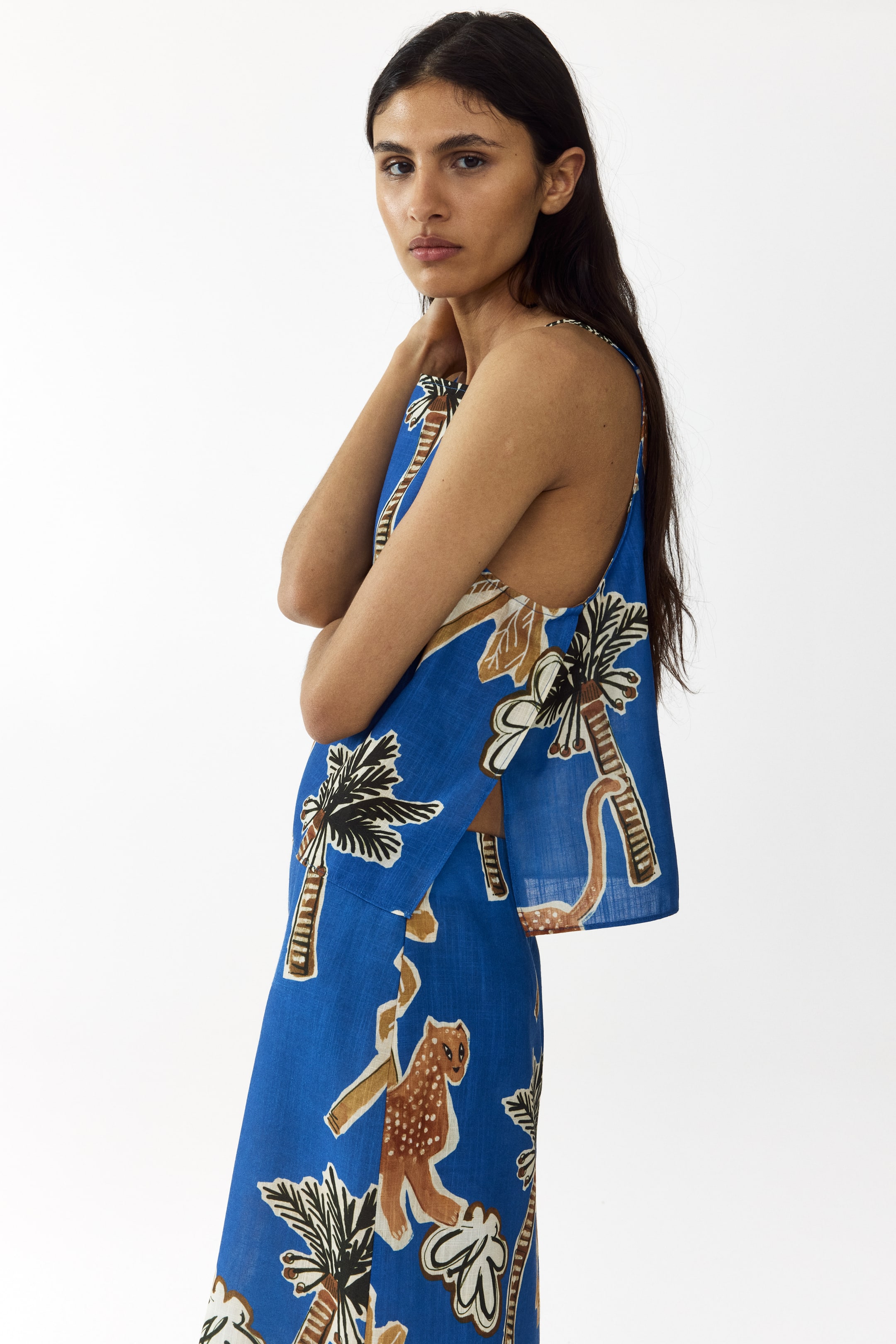 Agrandir l'image: Un haut court bleu, avec un imprimé tropical de palmiers et de léopards, est porté par le mannequin. Le haut est doté de fines bretelles et d'un ourlet droit avec des fentes de chaque côté, et il est assorti à un bas coordonné.