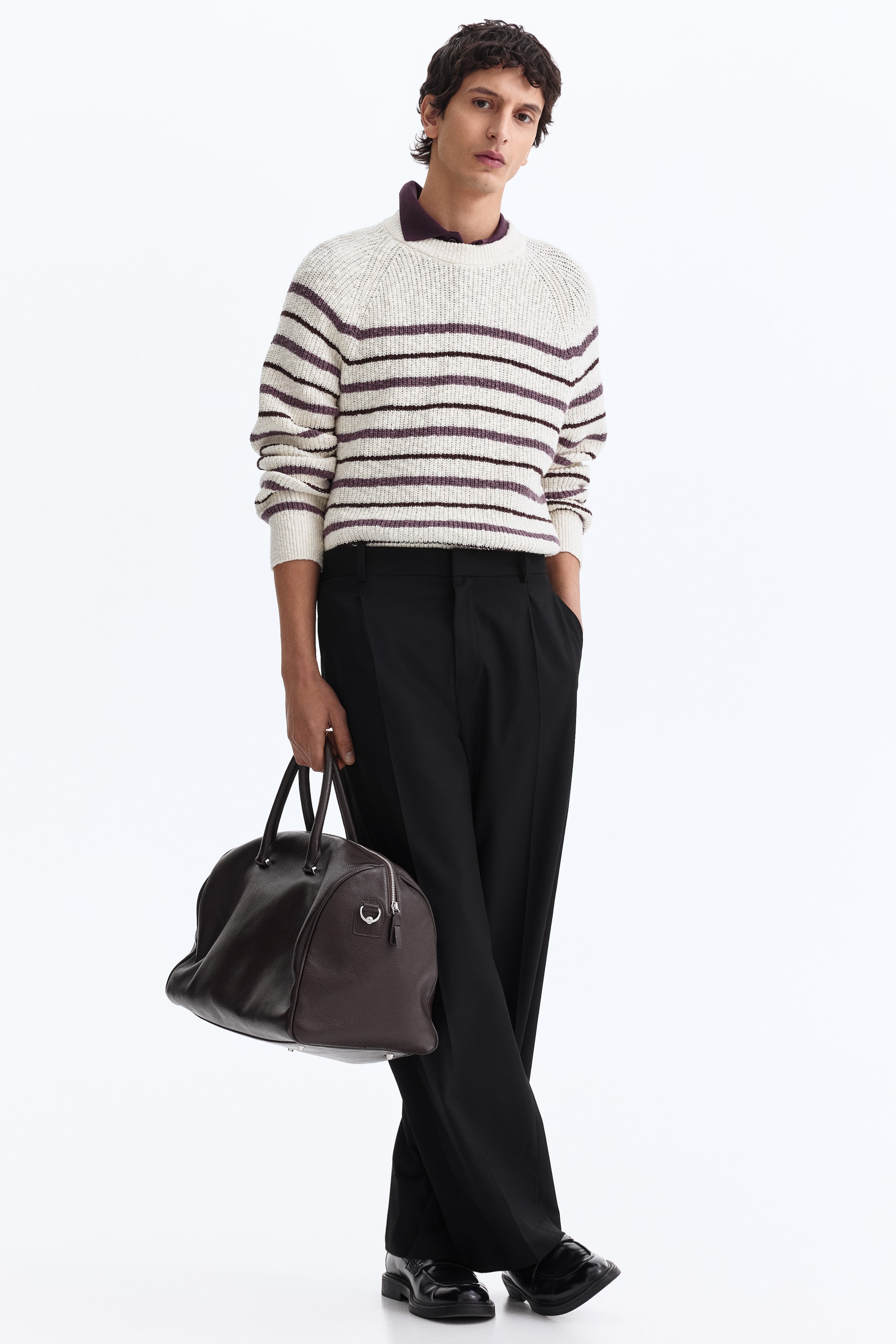 View larger image: A dark brown pebbled-leather duffle bag is held by its two top handles, angled slightly forward. It features a rounded shape and a silver-toned zipper closure running along the top.