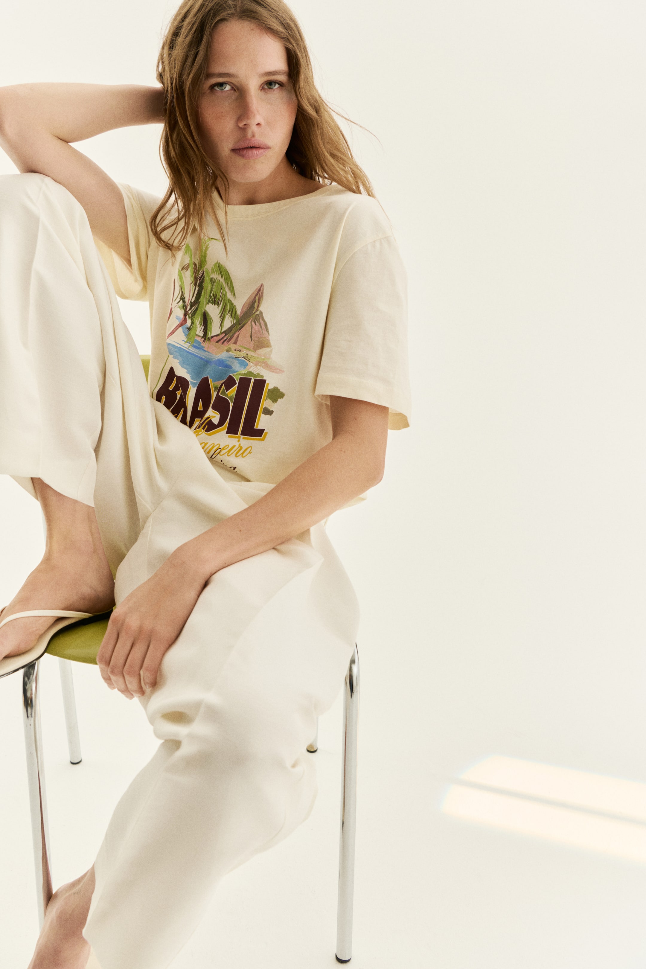 View larger image: A classic cream-colored t-shirt in cotton jersey is shown from the front, highlighting a vibrant tropical print motif with the word "BRASIL" and a scene of palm trees, mountains, and water. It features a round neckline, short sleeves, and a straight-cut hem.