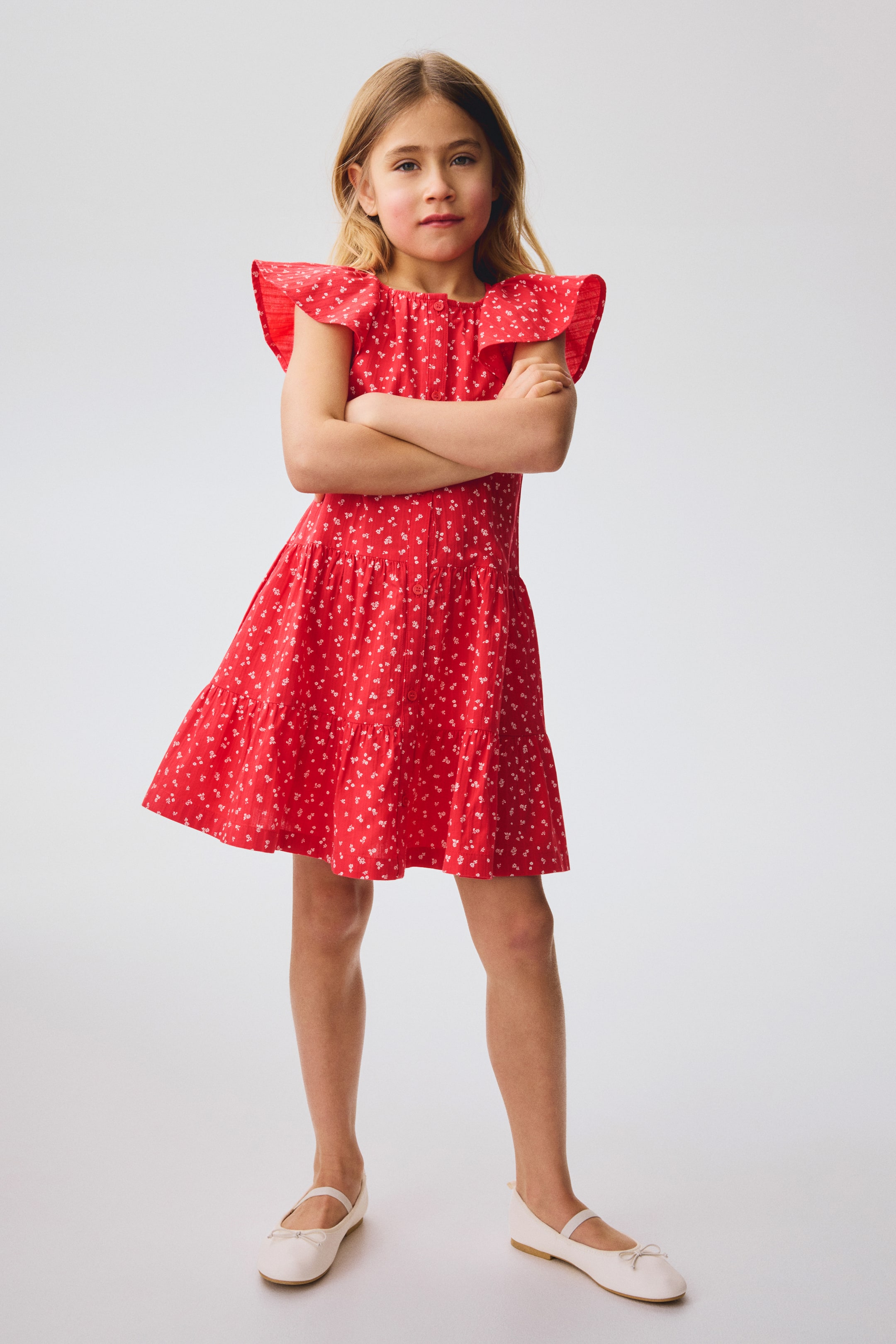 View larger image: An airy cotton seersucker dress adorned with a white floral pattern is displayed at the front, featuring a round neckline, buttons running down the front, and short ruffled sleeves. The skirt is crafted with gathered tiers, adding volume.