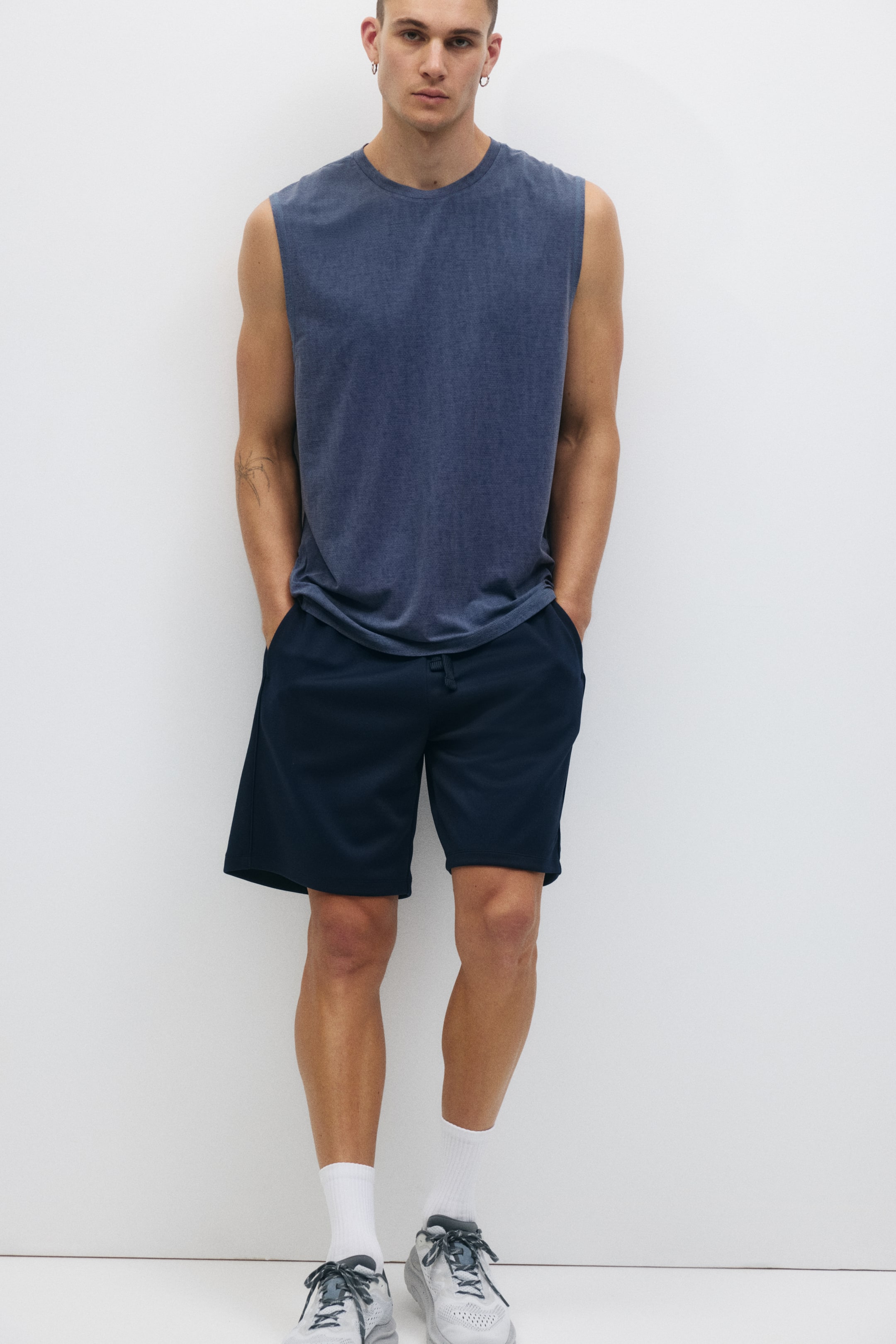 View larger image: A muted blue sleeveless t-shirt with a crew neck is showcased, paired with dark blue shorts. The shorts include side pockets and an elastic waistband with a visible drawstring, reaching above the knee.