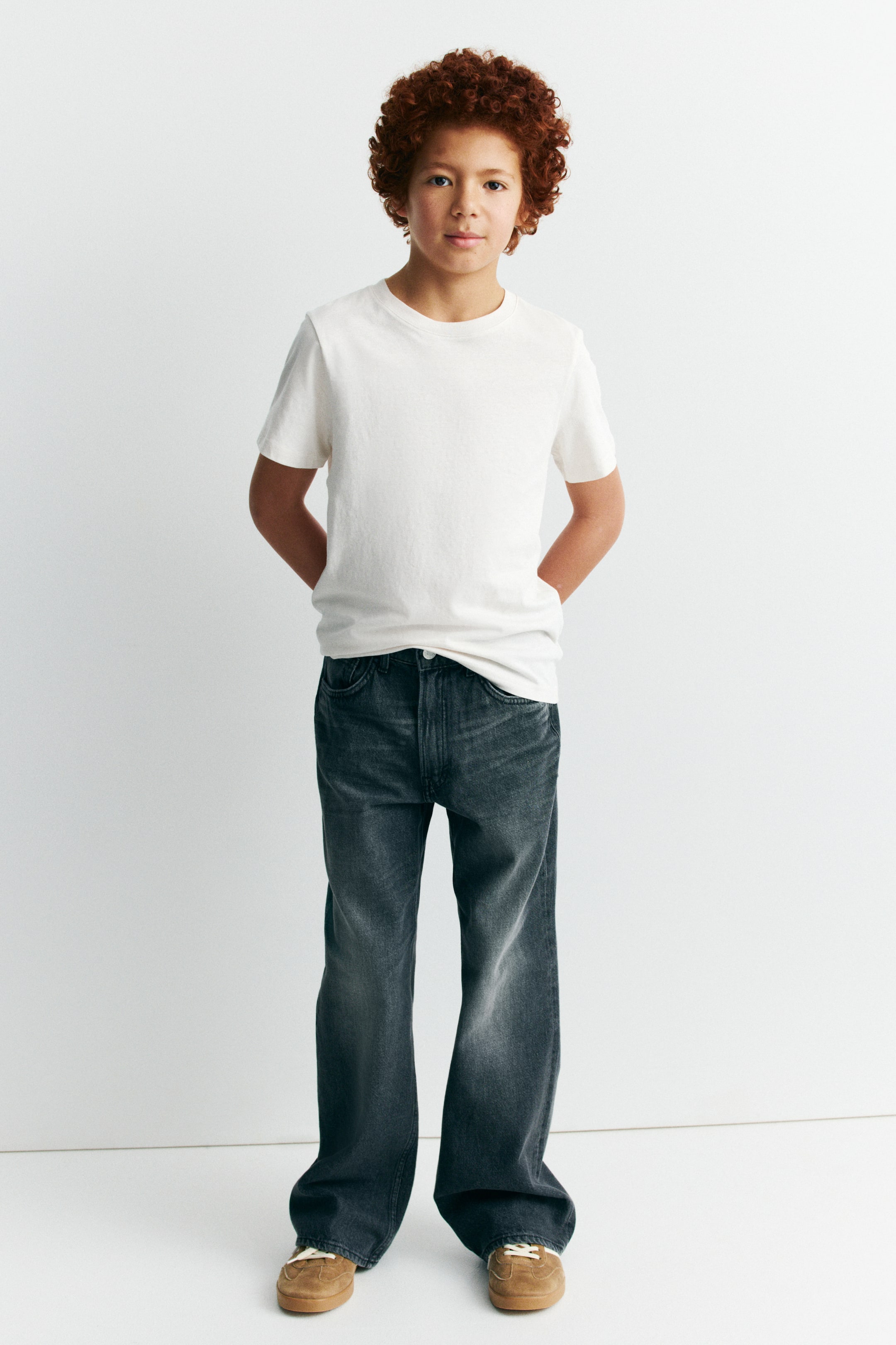 Ver imagem maior: Calças de ganga cinza-escuro de perna larga são apresentadas de frente, com um efeito desbotado e bolsos frontais. As calças de comprimento total estão ligeiramente acumuladas nos tornozelos e são combinadas com uma t-shirt branca metida na cintura.