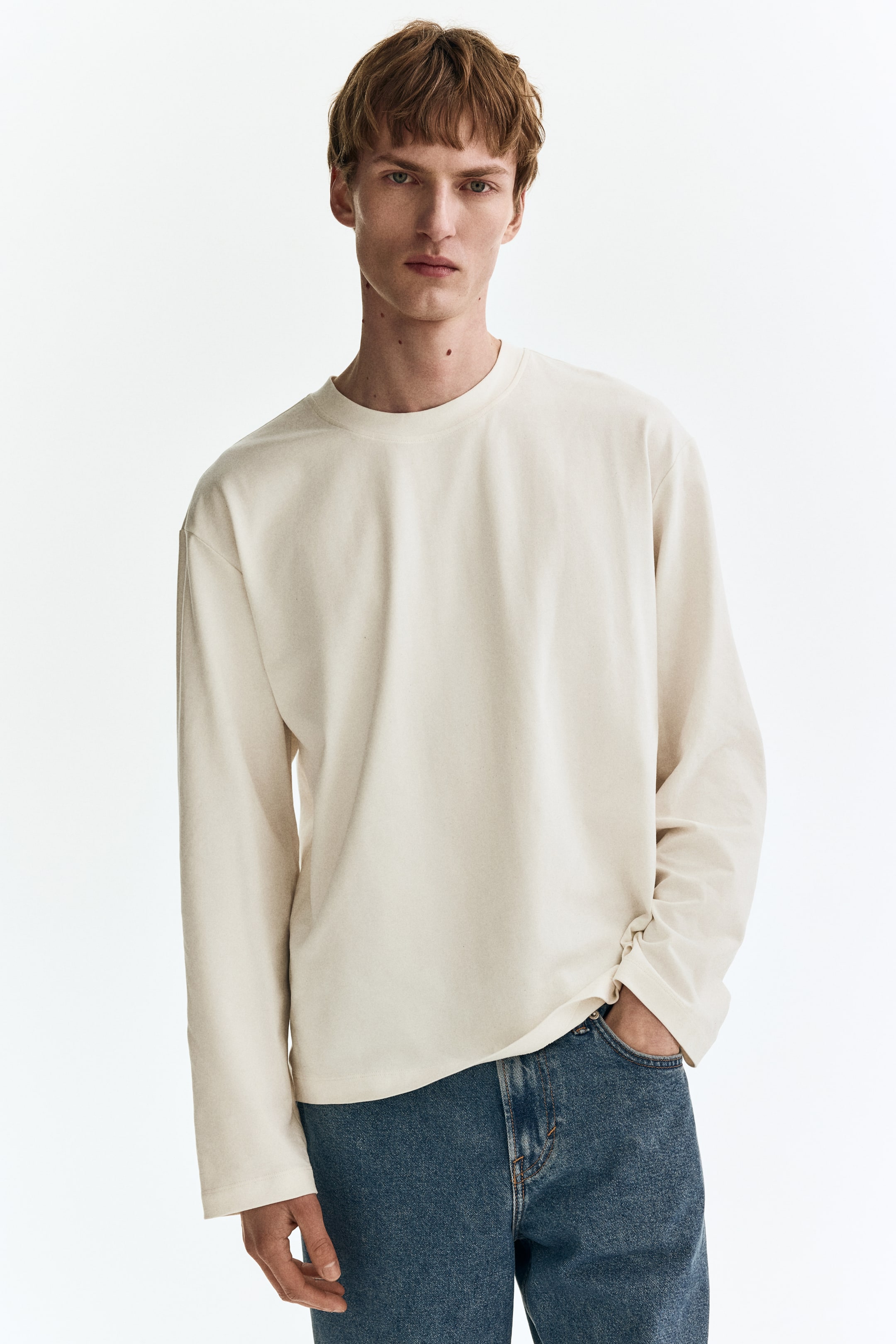 Visualizza immagine più grande: Una t-shirt bianco sporco a maniche lunghe presenta una vestibilità rilassata con scollo rotondo e maniche lunghe. È caratterizzata da polsini dritti e un orlo inferiore diritto.