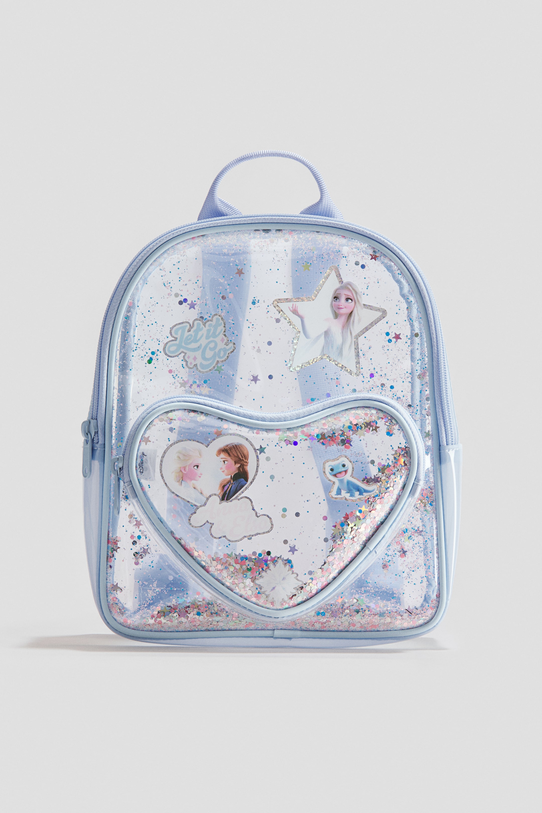 Grösseres Bild ansehen: Ein klarer hellblauer Rucksack wird von vorne präsentiert, mit einem Hauptfach mit Reissverschluss und einer herzförmigen Fronttasche mit Reissverschluss. Beide Fächer sind mit irisierendem Glitzer und Konfetti gefüllt, wobei Bilder von Frozen-Charakteren und der Text "Let it Go" innerhalb der klaren Paneele sichtbar sind.