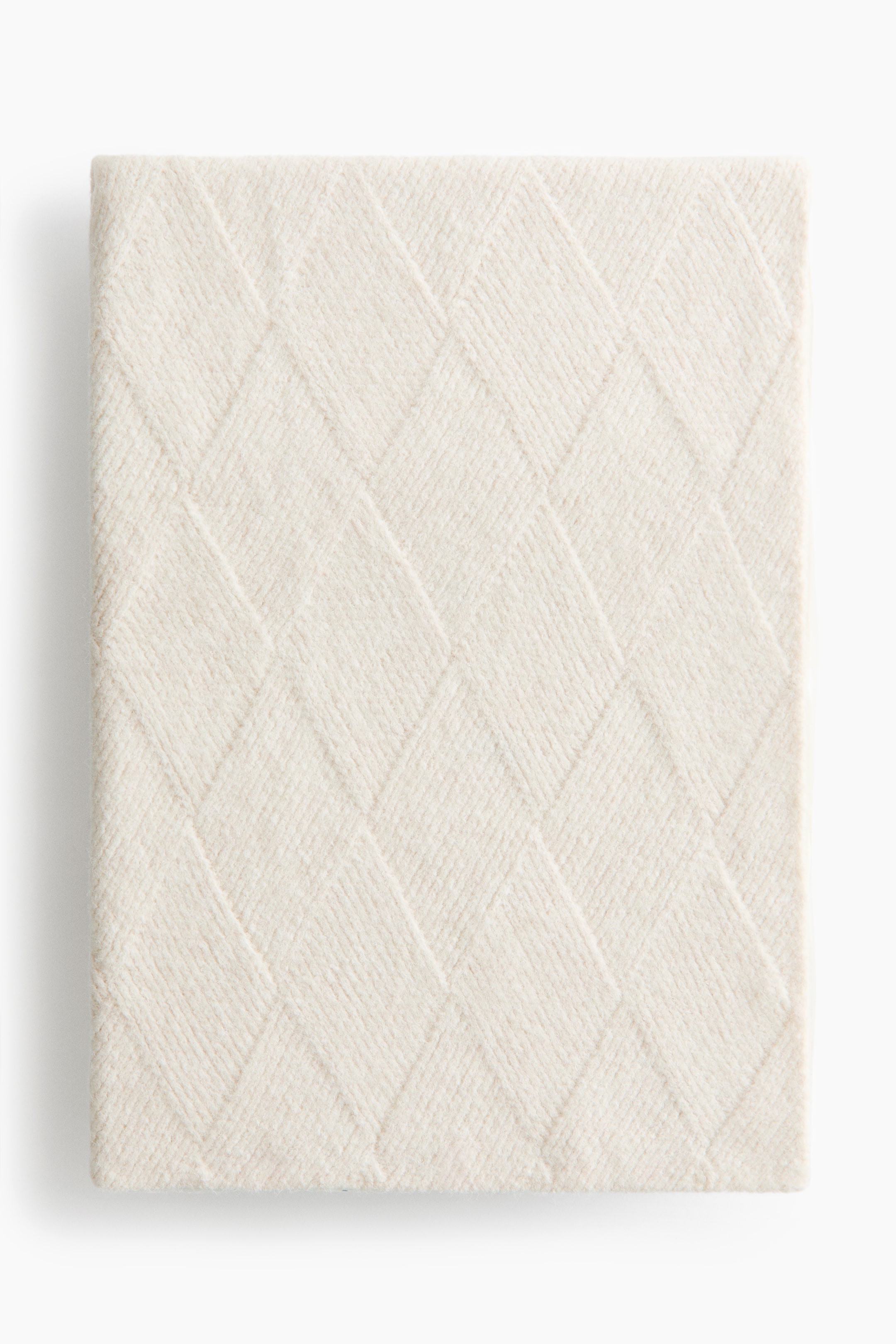 View larger image: A cream-colored blanket is folded into a square, showcasing a soft knit texture with a textured diamond pattern across its front surface.
