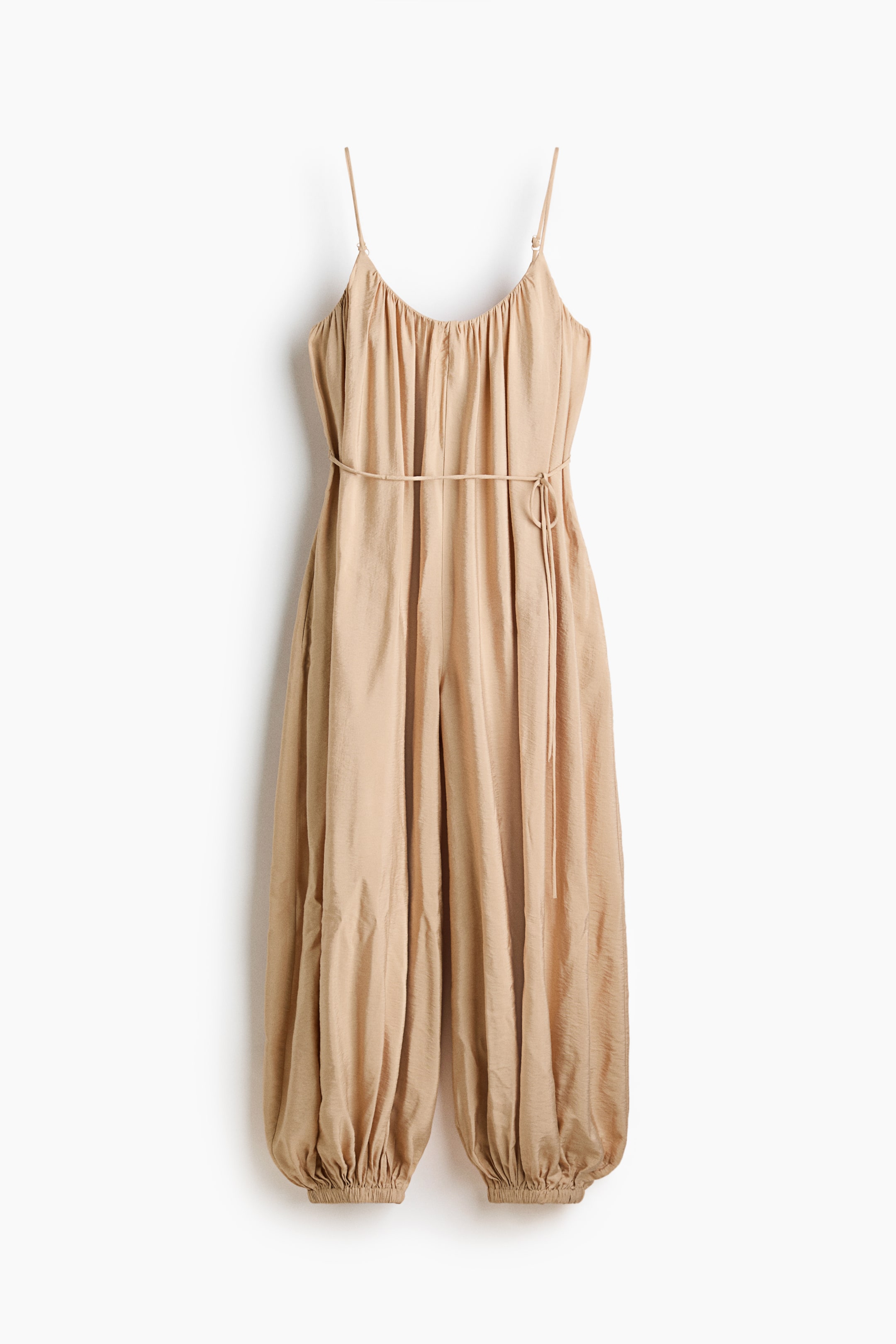 View larger image: Presenting a loose-fit jumpsuit from the front, it showcases a gathered scoop neckline, narrow adjustable shoulder straps, and spaghetti ties at the waist. The design is completed with ankle-length balloon legs, ending in elasticated hems.