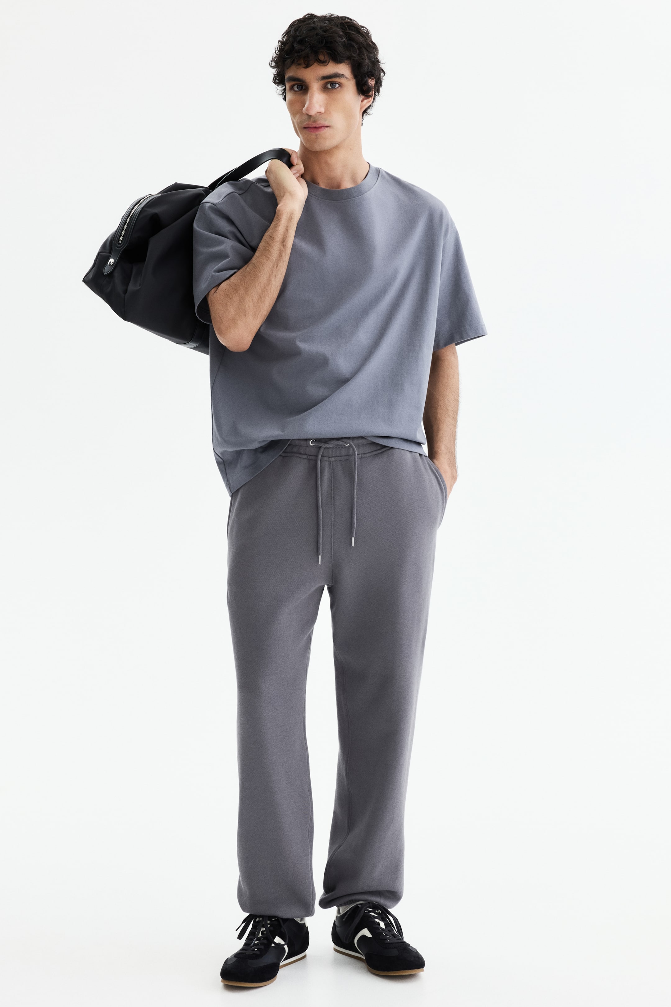 이미지 확대 보기: 연한 회색의 오버사이즈 크루넥 티셔츠가 짙은 회색의 릴랙스 핏 스웨트팬츠와 함께 착용되고 있으며, 허리끈이 보이는 허리와 오픈 헴이 특징입니다.