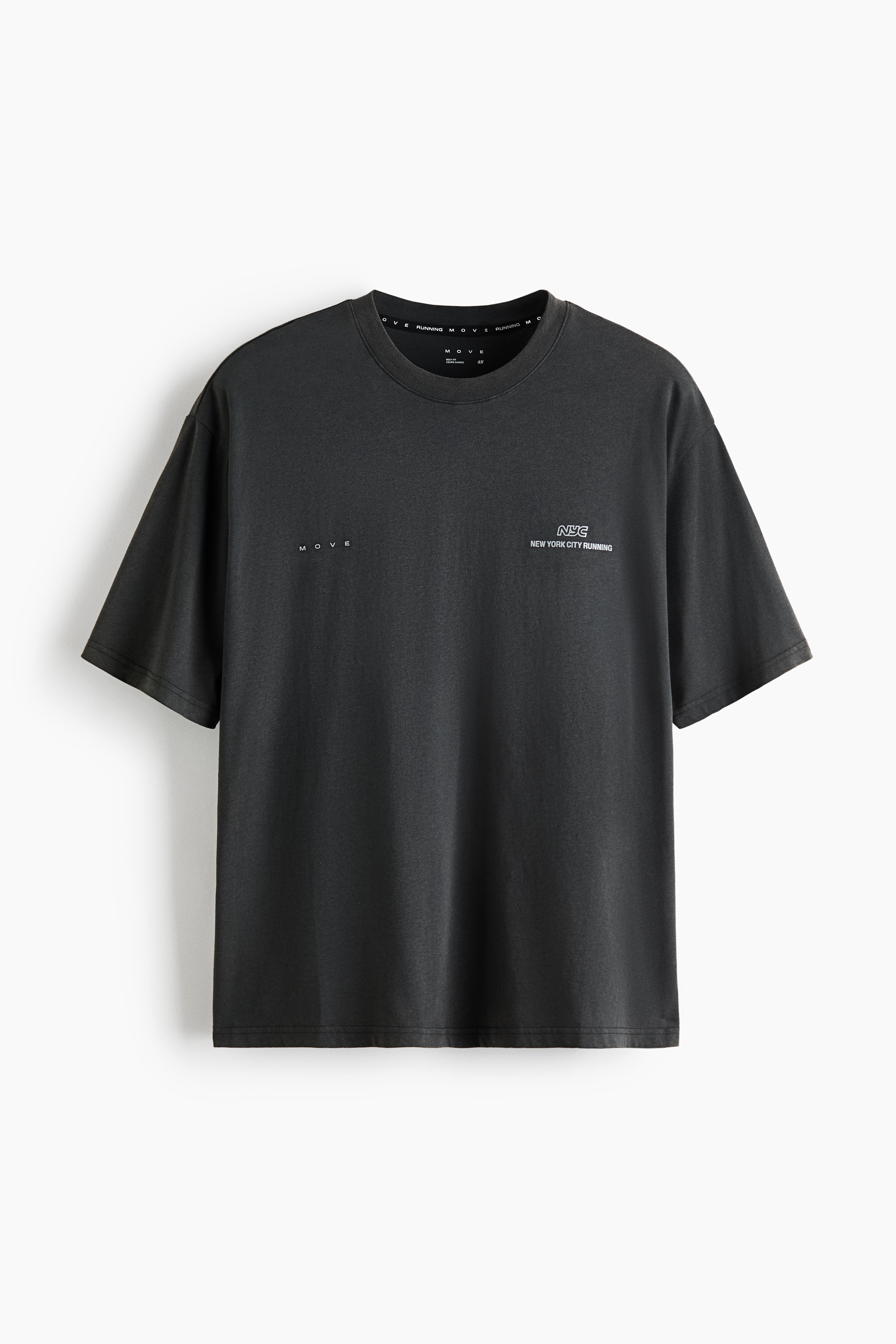 A black short-sleeved T-shirt featuring a small white chest graphic is worn by the model over a white long-sleeved top and paired with black athletic compression shorts. This layered look is styled with white crew socks and light grey running shoes.