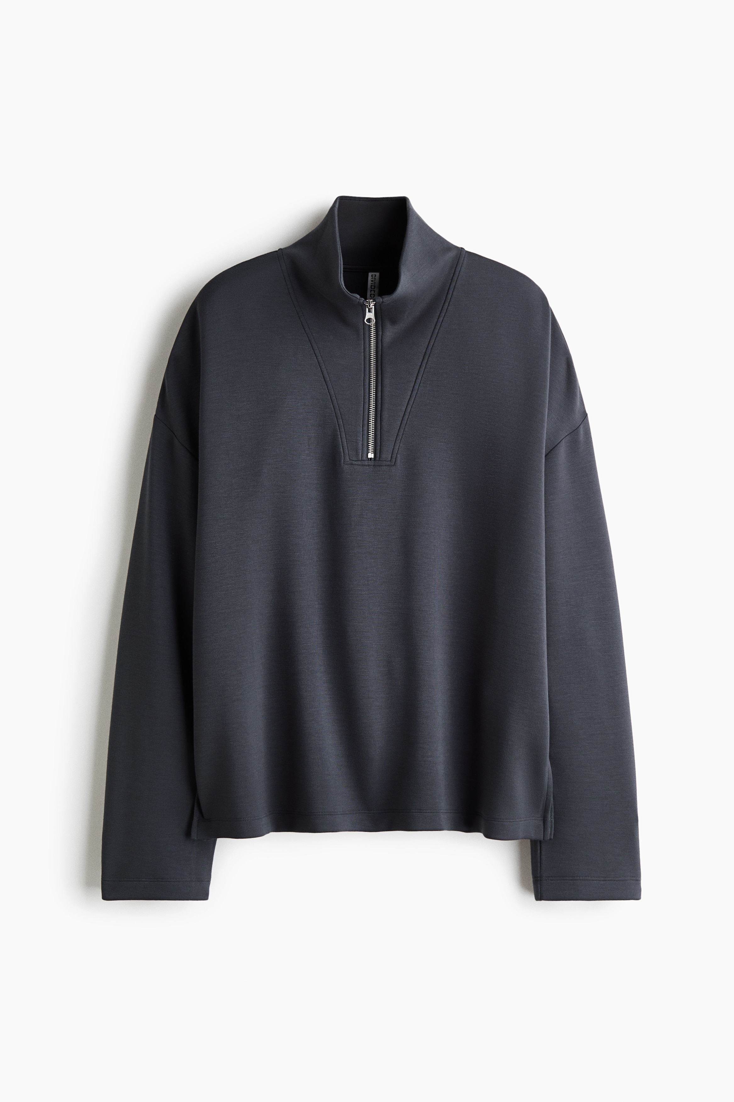 A dark grey lounge set, comprising a half-zip sweatshirt and matching wide-leg trousers, is worn by the model. The model is holding the hem of the sweatshirt up to reveal a striped top layered underneath.