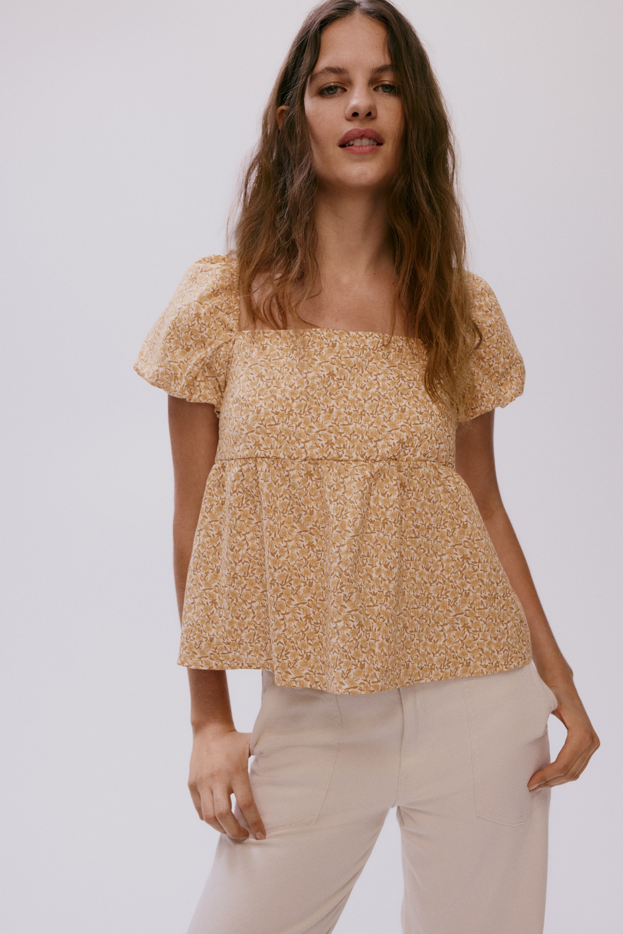 Ampliar la imagen: "Una blusa de escote cuadrado con un estampado floral en amarillo y beige, mangas cortas abullonadas y un corpiño ajustado que se ensancha en un dobladillo peplum."